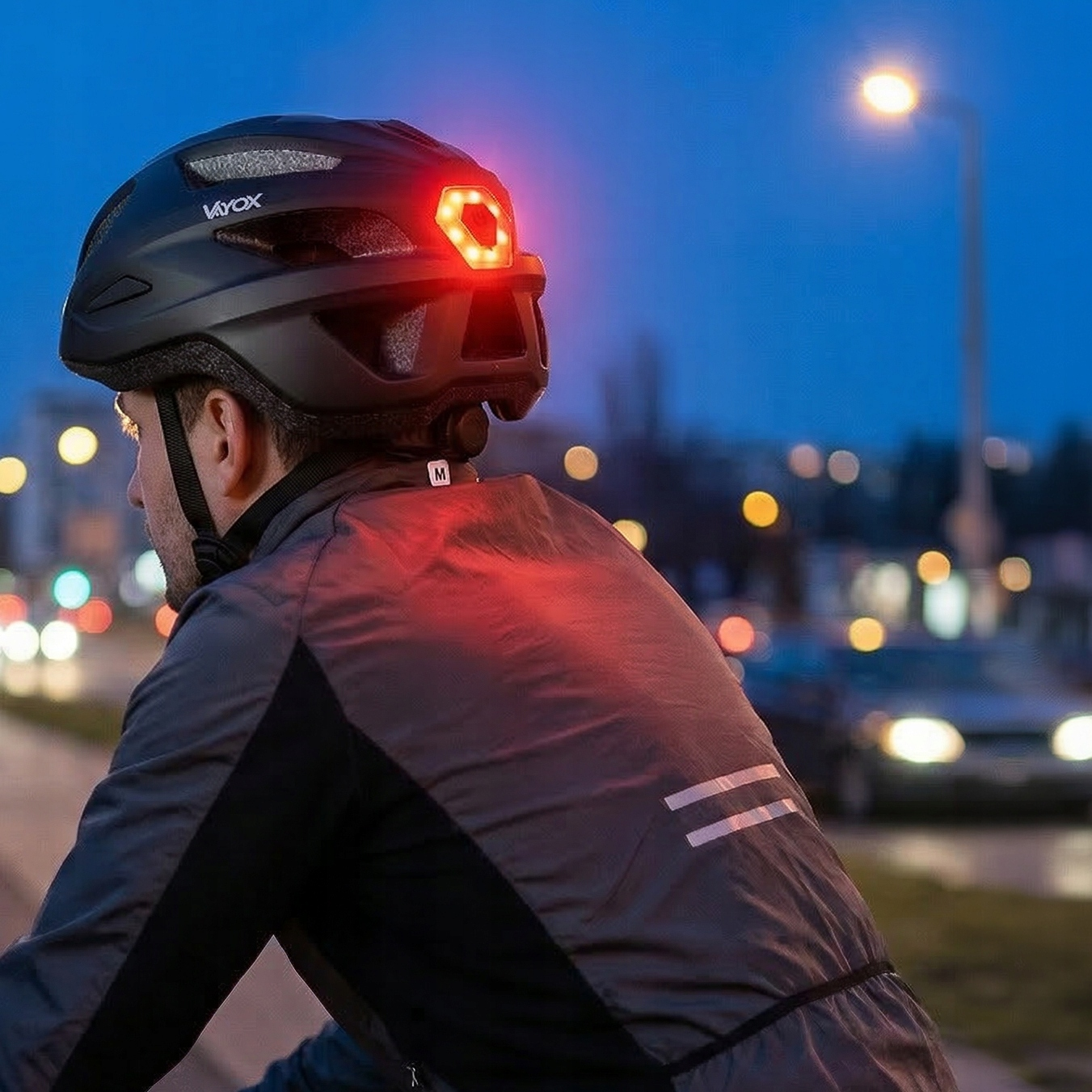 Kolarz w czarnym kasku z czerwonym światłem tylnym o zmierzchu, widok miasta.