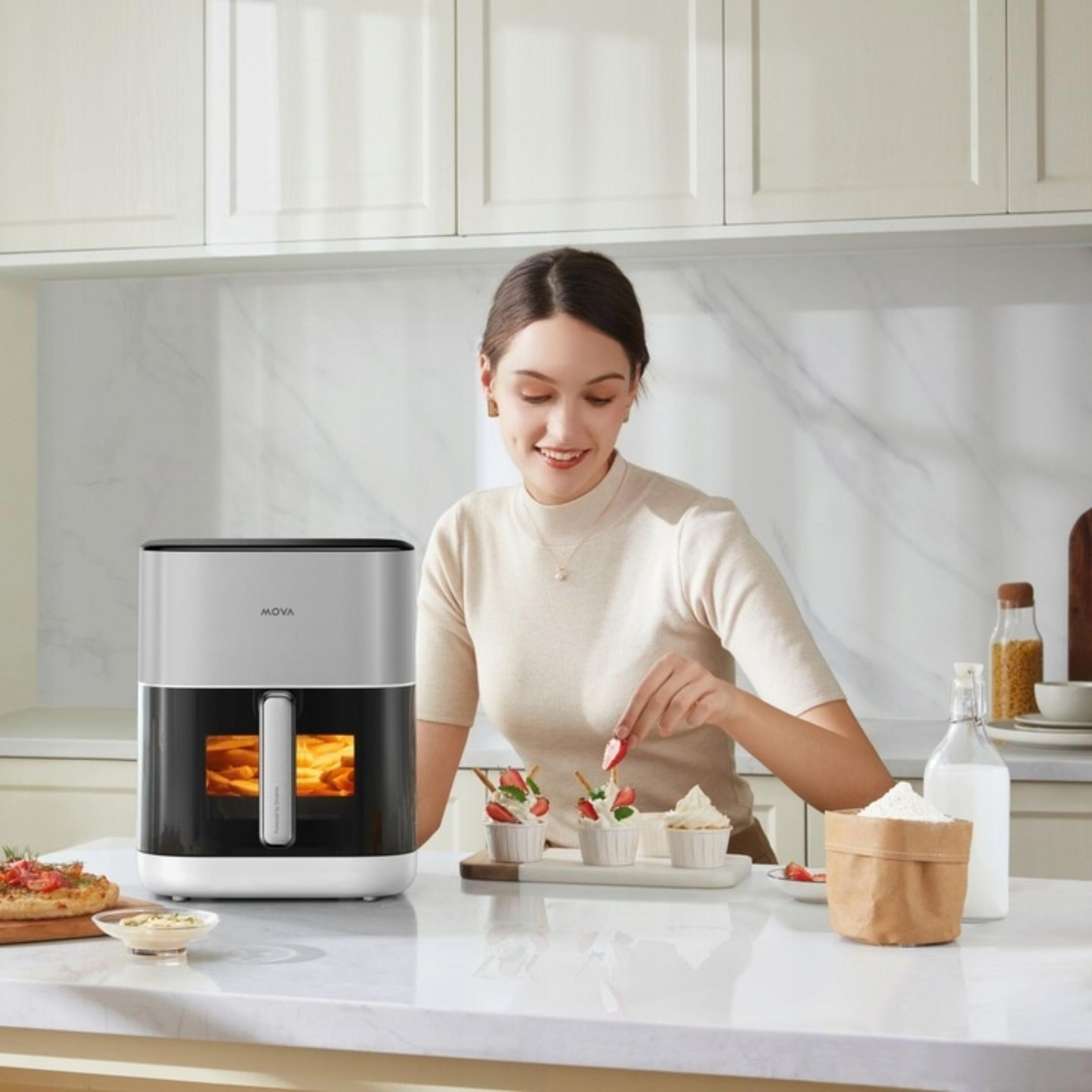 Kobieta dekoruje babeczki w kuchni z frytkownicą i pizzą.