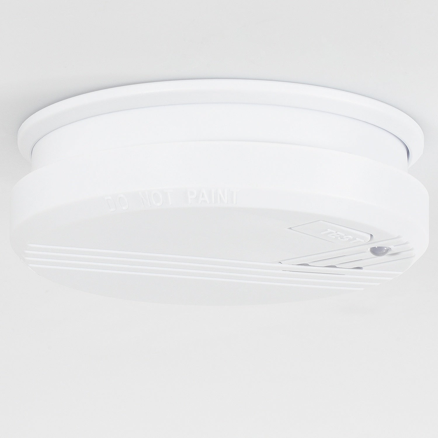 Een witte rookmelder is op een wit plafond gemonteerd. Hij heeft een testknop.