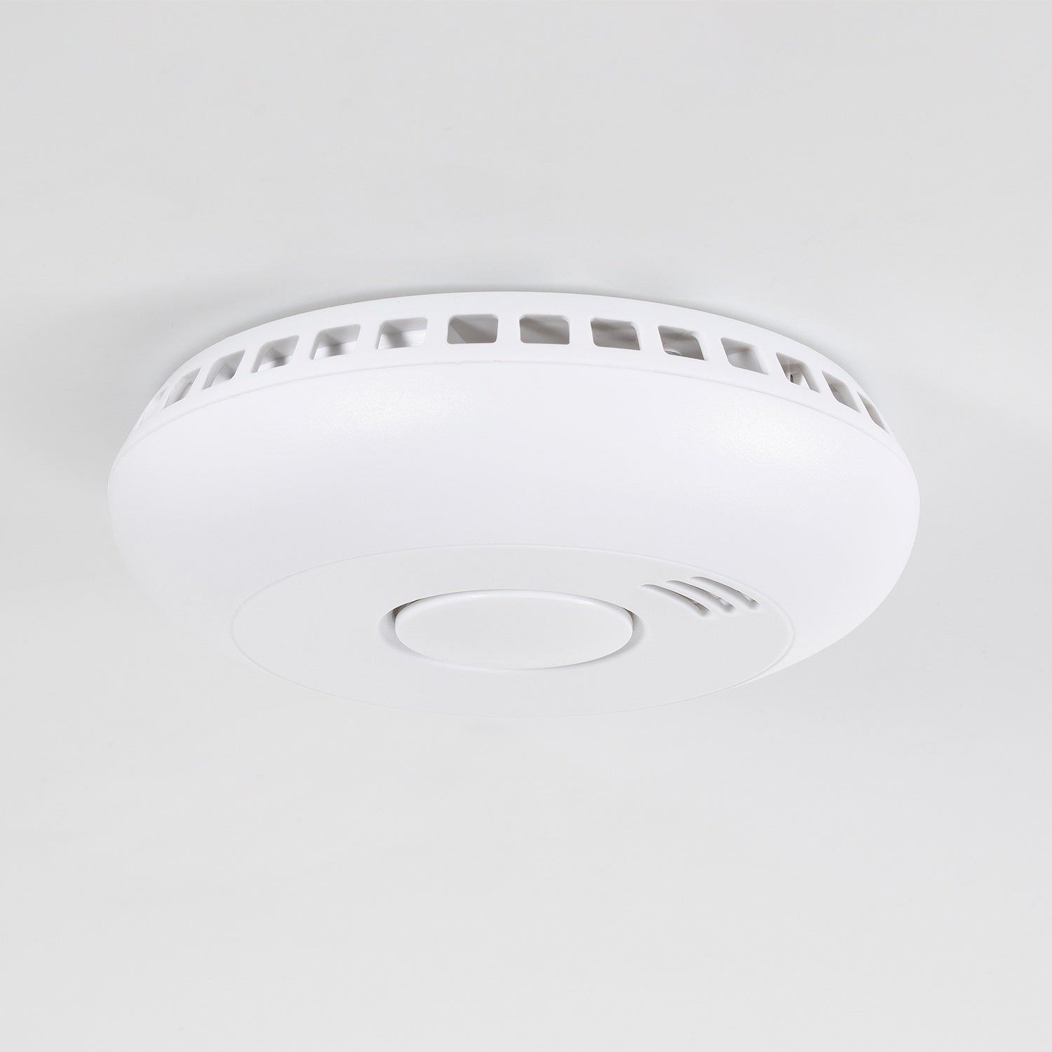 A white smoke detector is mounted on a white ceiling.