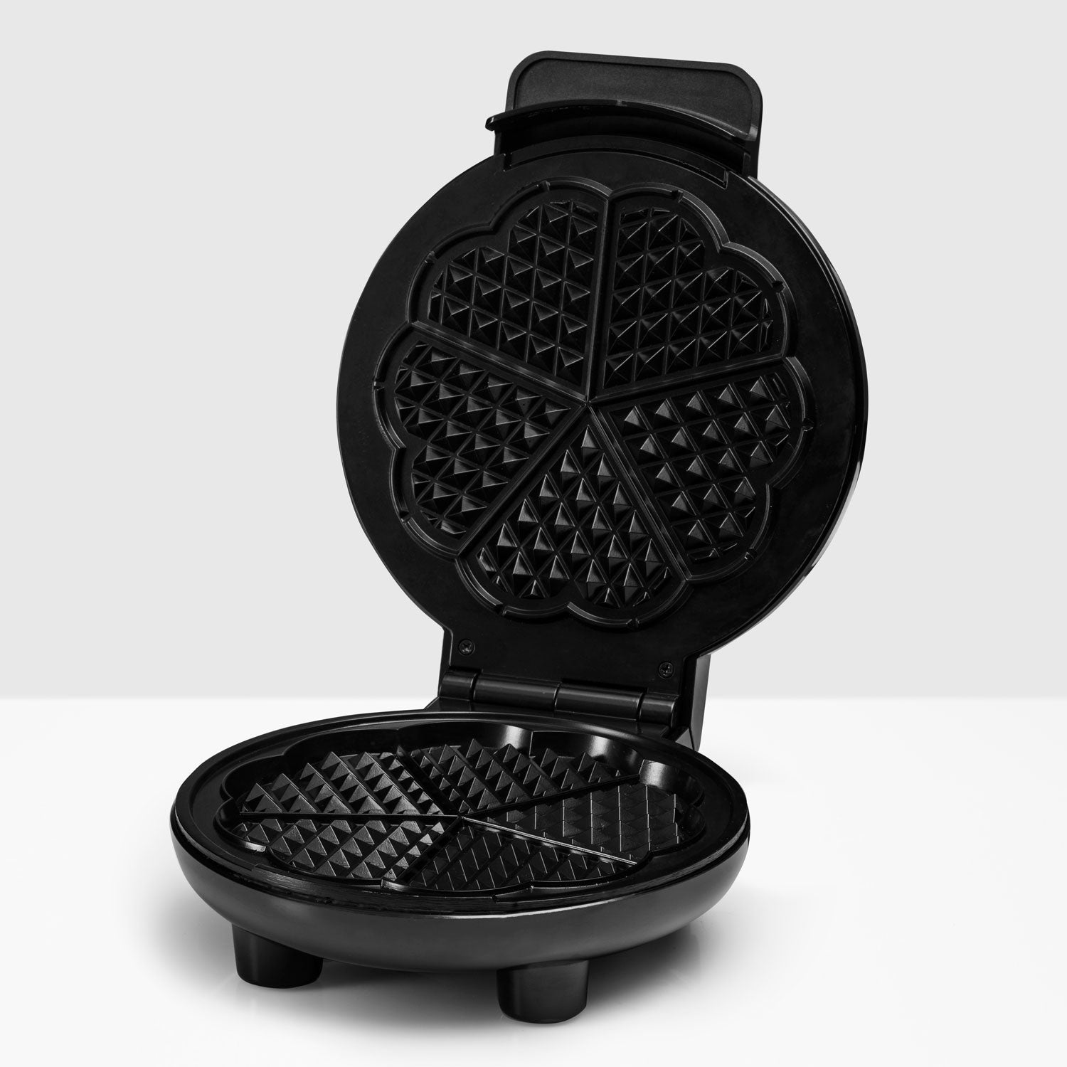 A black, open waffle maker with heart-shaped indentations for waffles.