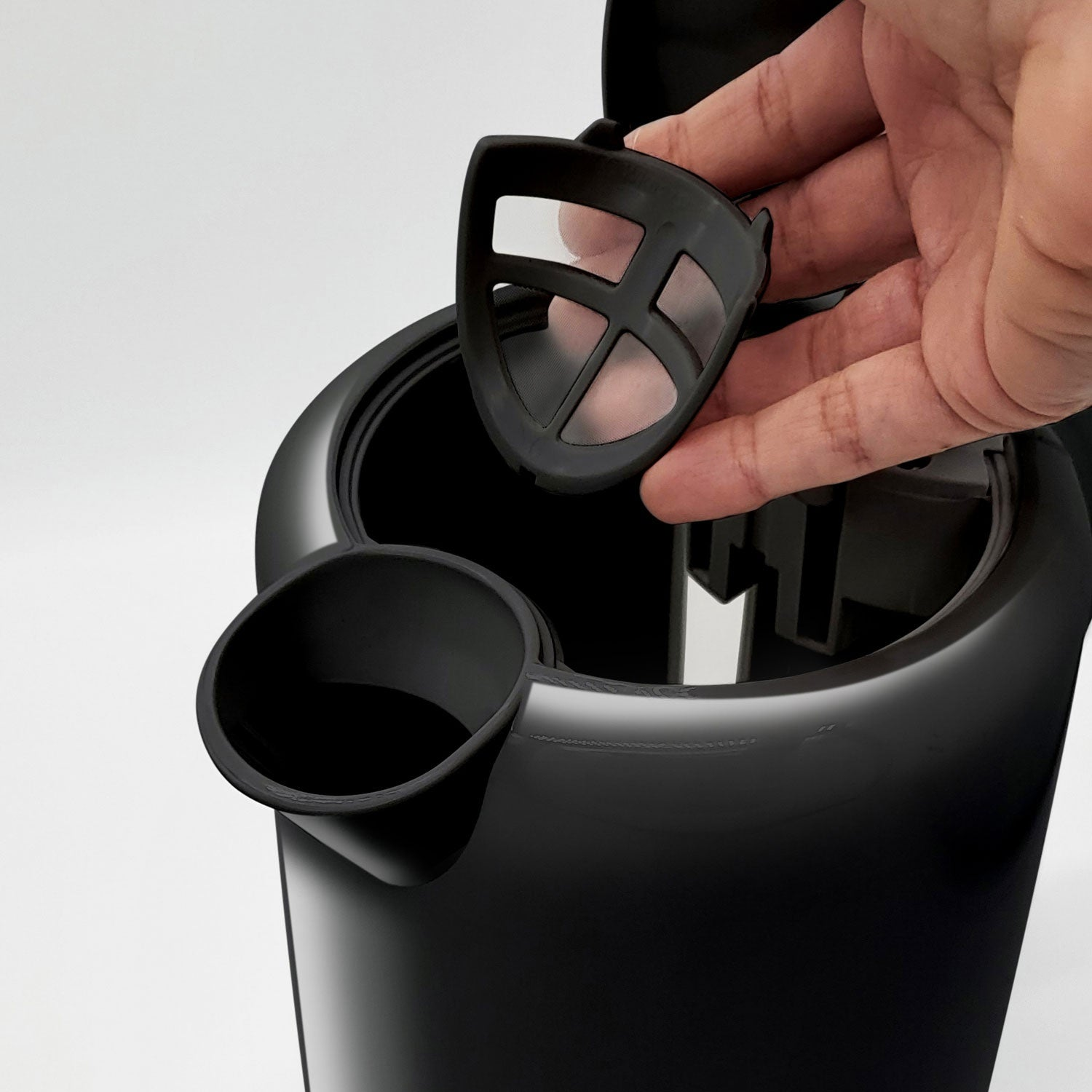 A hand holds a black plastic filter insert over a black container.
