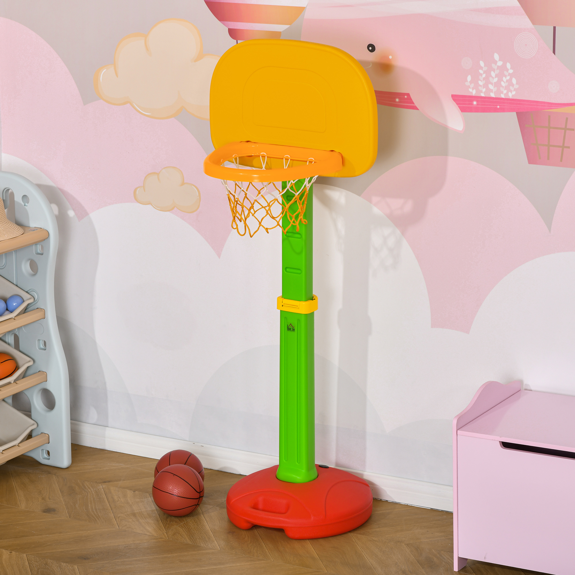 Una colorida canasta de baloncesto infantil se alza sobre un suelo de madera frente a una pared con motivos de nubes.