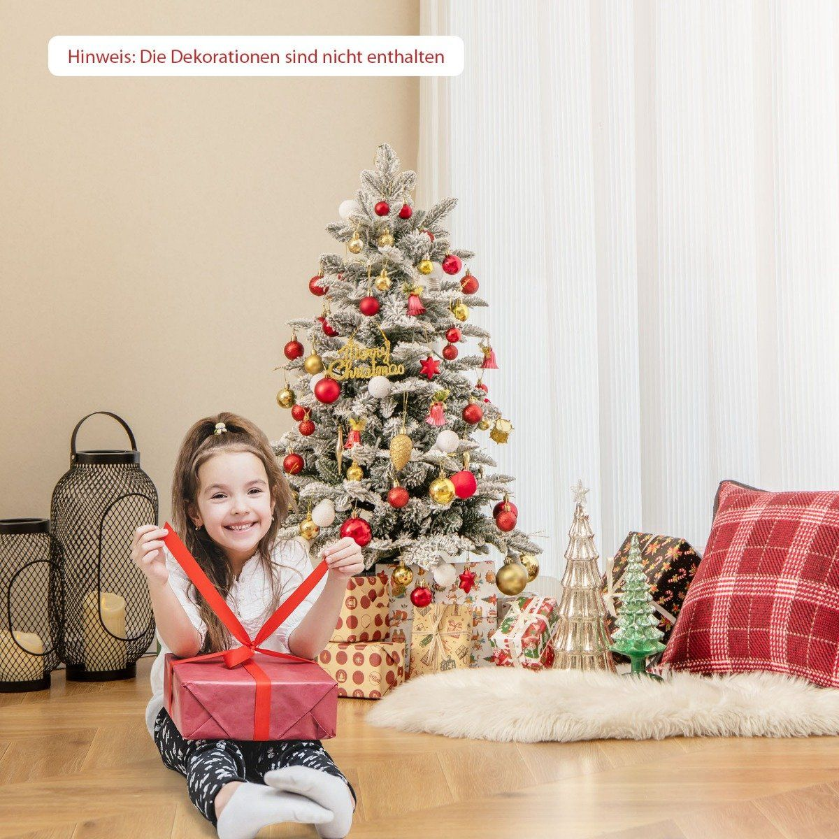 Een meisje opent een cadeau voor een kerstboom met rode en gouden ornamenten.