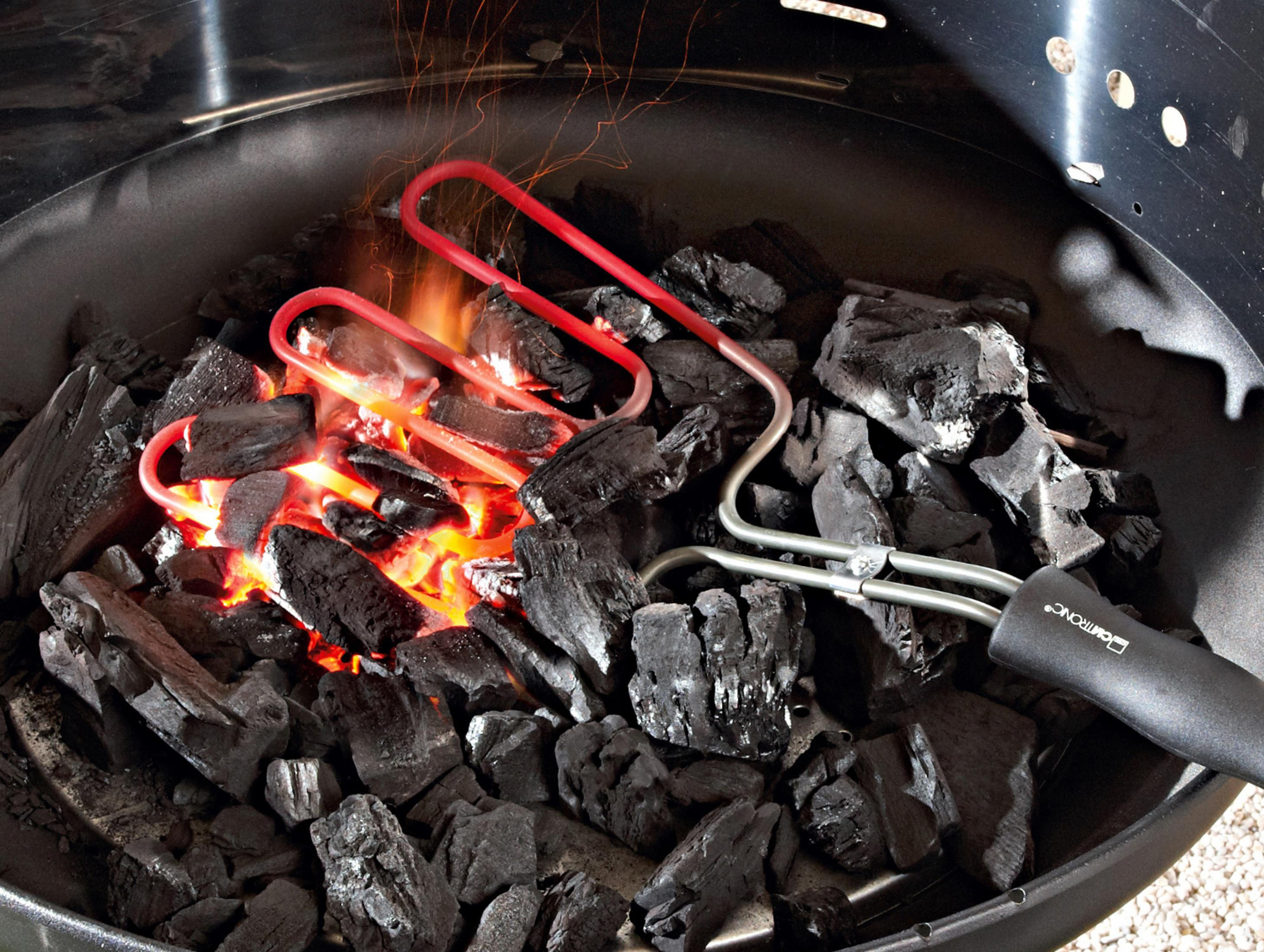 Żarzący się węgiel drzewny w grillu z czerwonymi grzałkami i szczypcami.