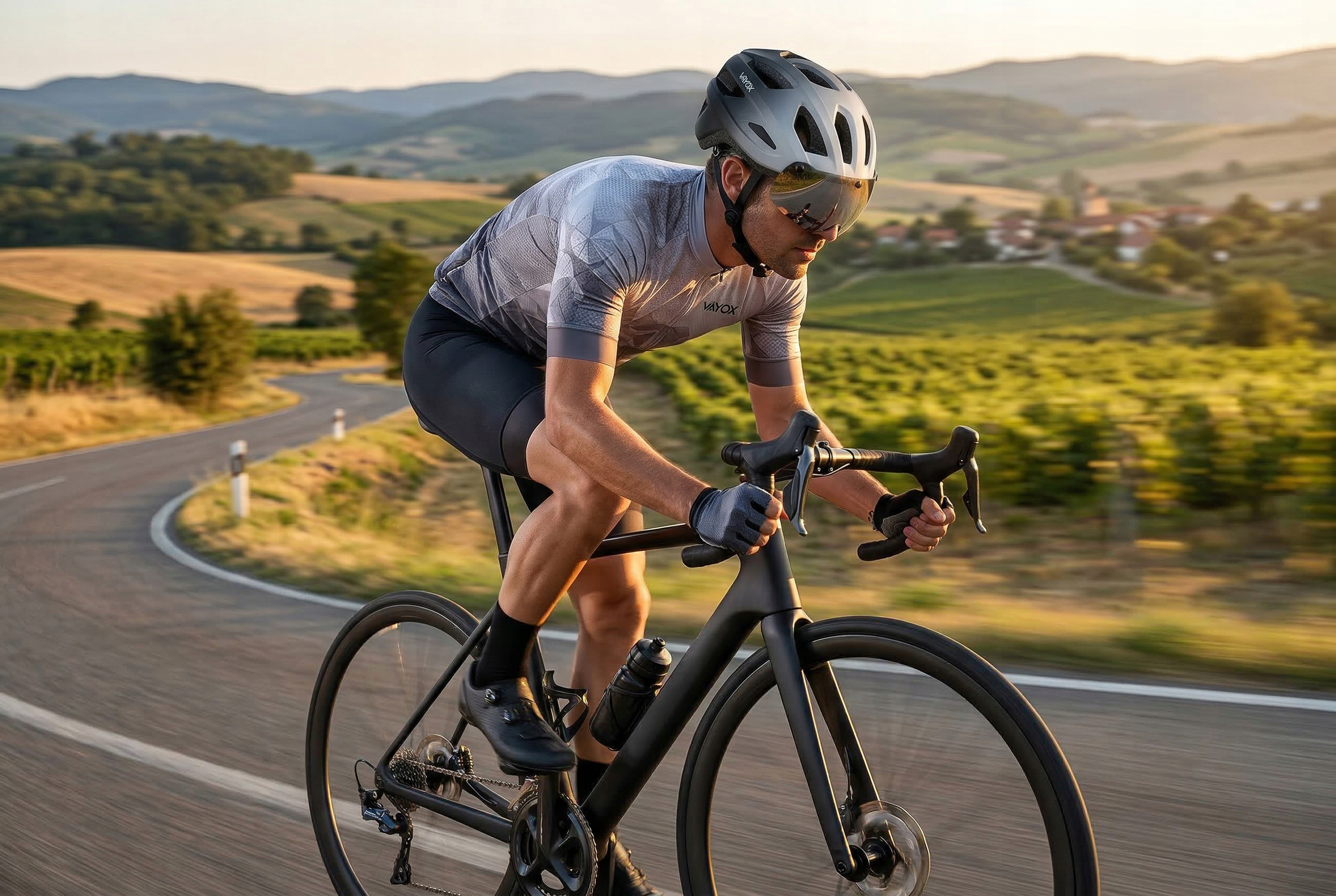 Kolarz na krętej drodze przez pofałdowane wzgórza o zachodzie słońca.