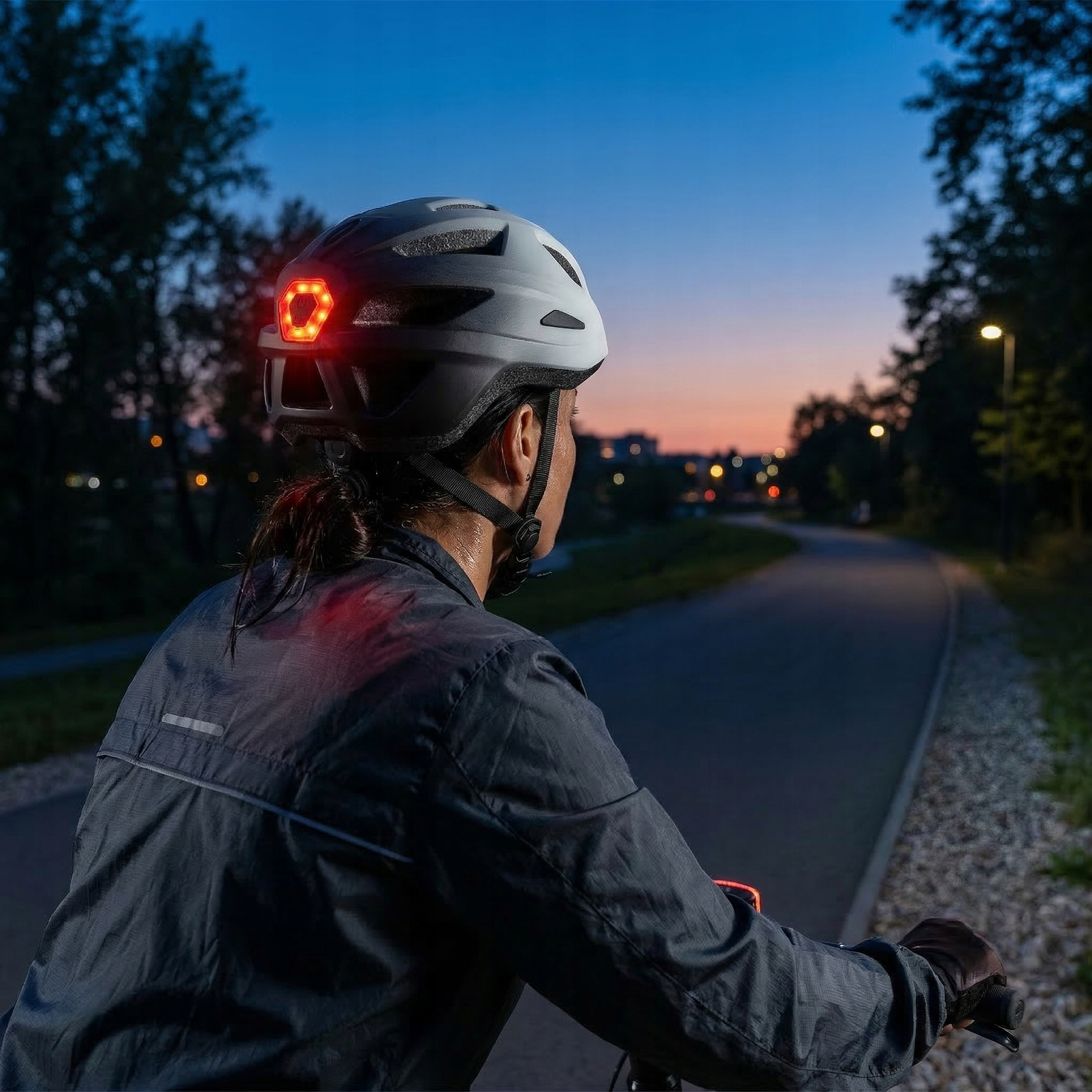 Kolarz w kasku z podświetlaną tylną lampką na ścieżce rowerowej o zmierzchu.