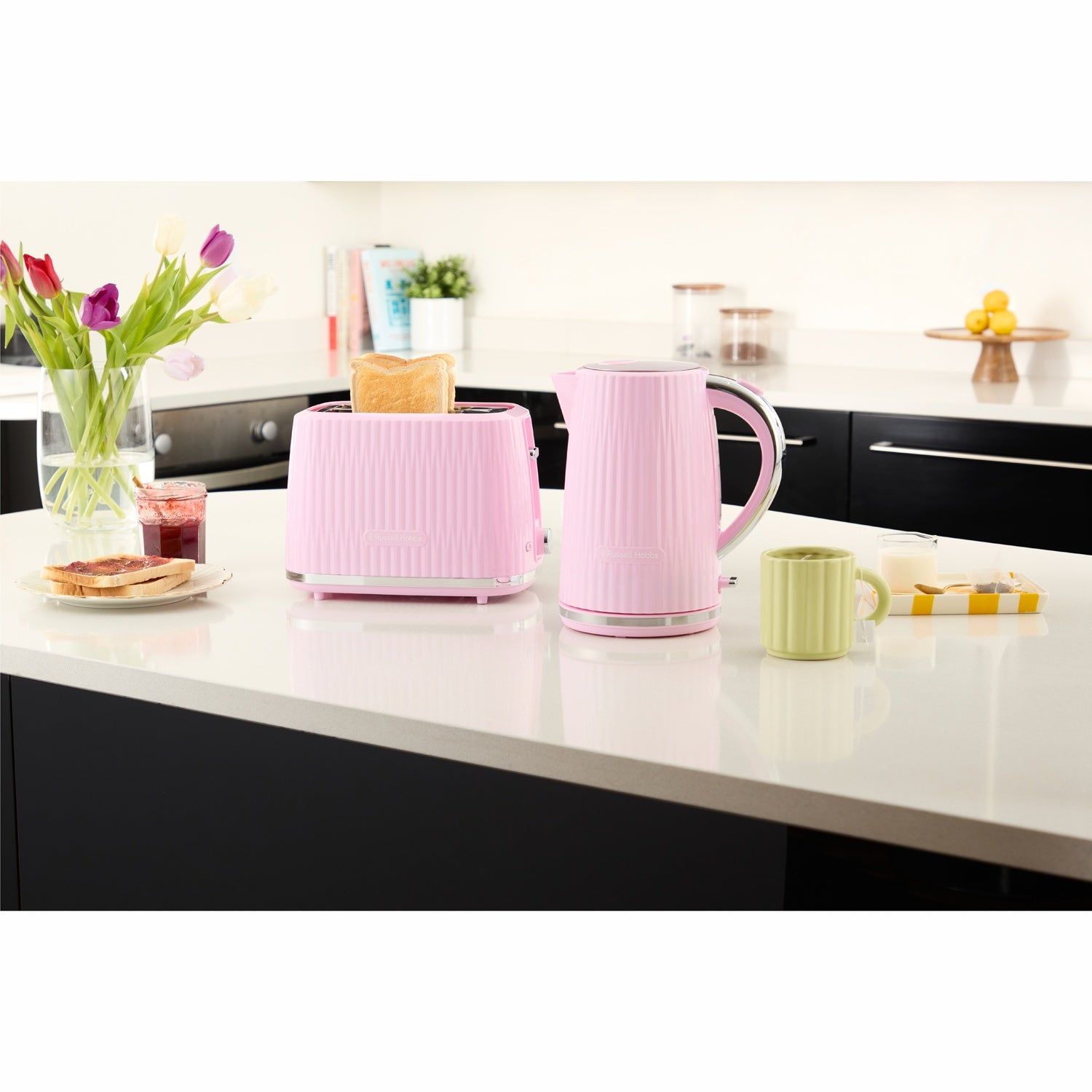 Roze broodrooster en waterkoker op een aanrecht met toast, jam, bloemen en een mok.