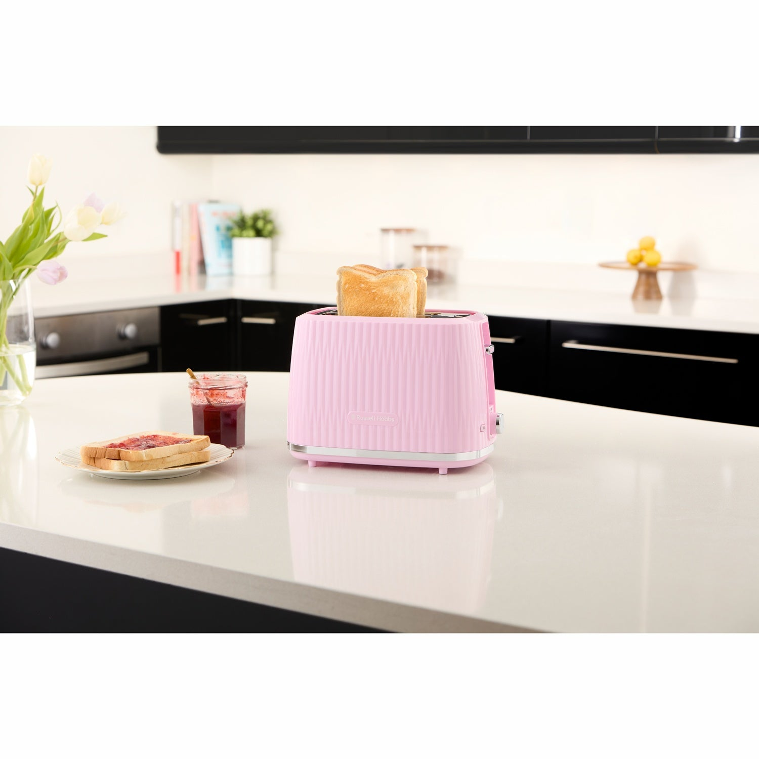 Een roze broodrooster met toast, jam en brood op een wit aanrechtblad.