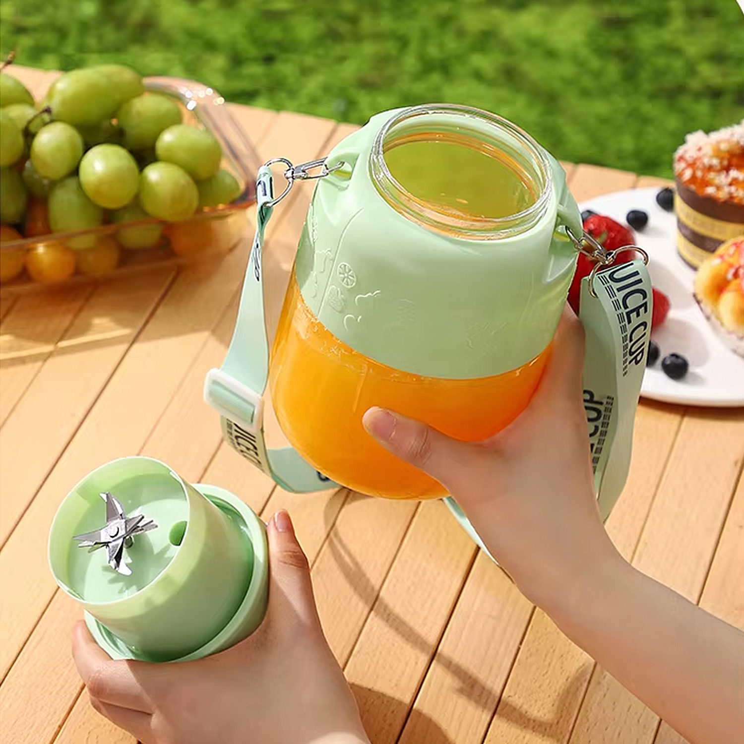 Eine Person hält einen tragbaren Mixer mit Orangesaft, daneben Trauben und Kuchen.