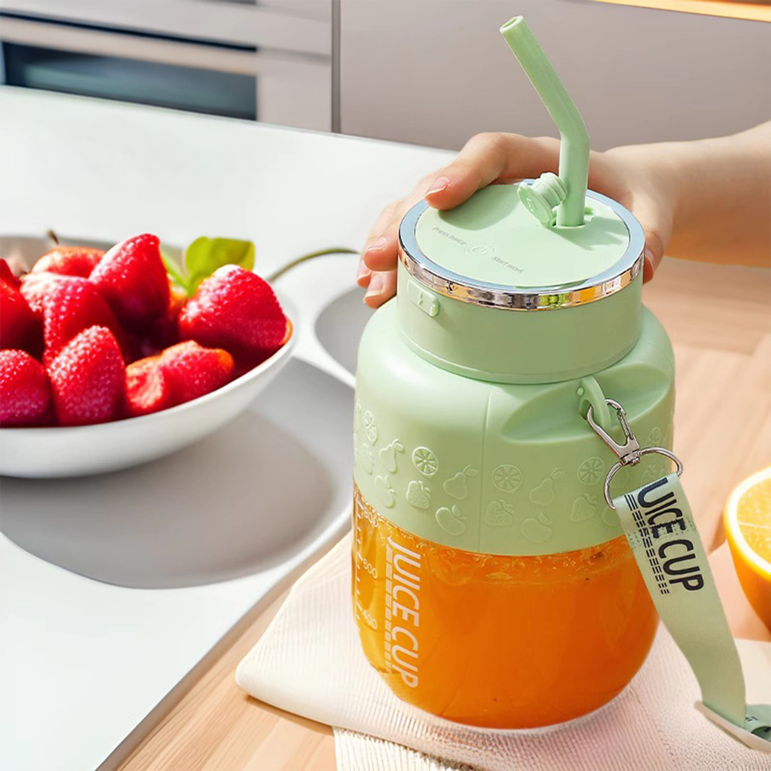 Grüne Saftbecher mit Strohhalm, neben einer Schüssel mit Erdbeeren und einer halben Zitrone.