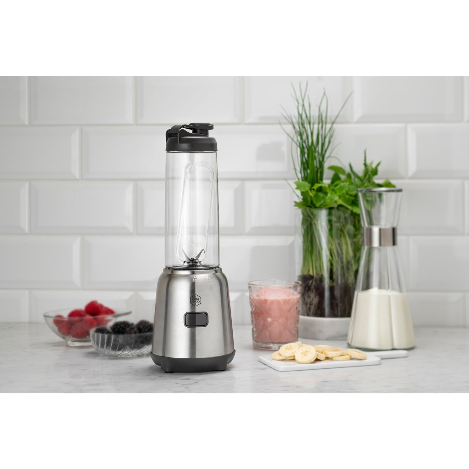 A silver blender with a glass container sits on a marble countertop next to berries, bananas, and drinks.