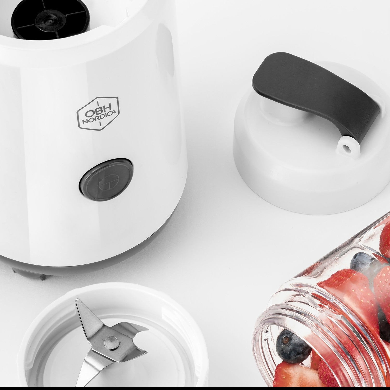 A white blender with a transparent cup filled with strawberries and blueberries.