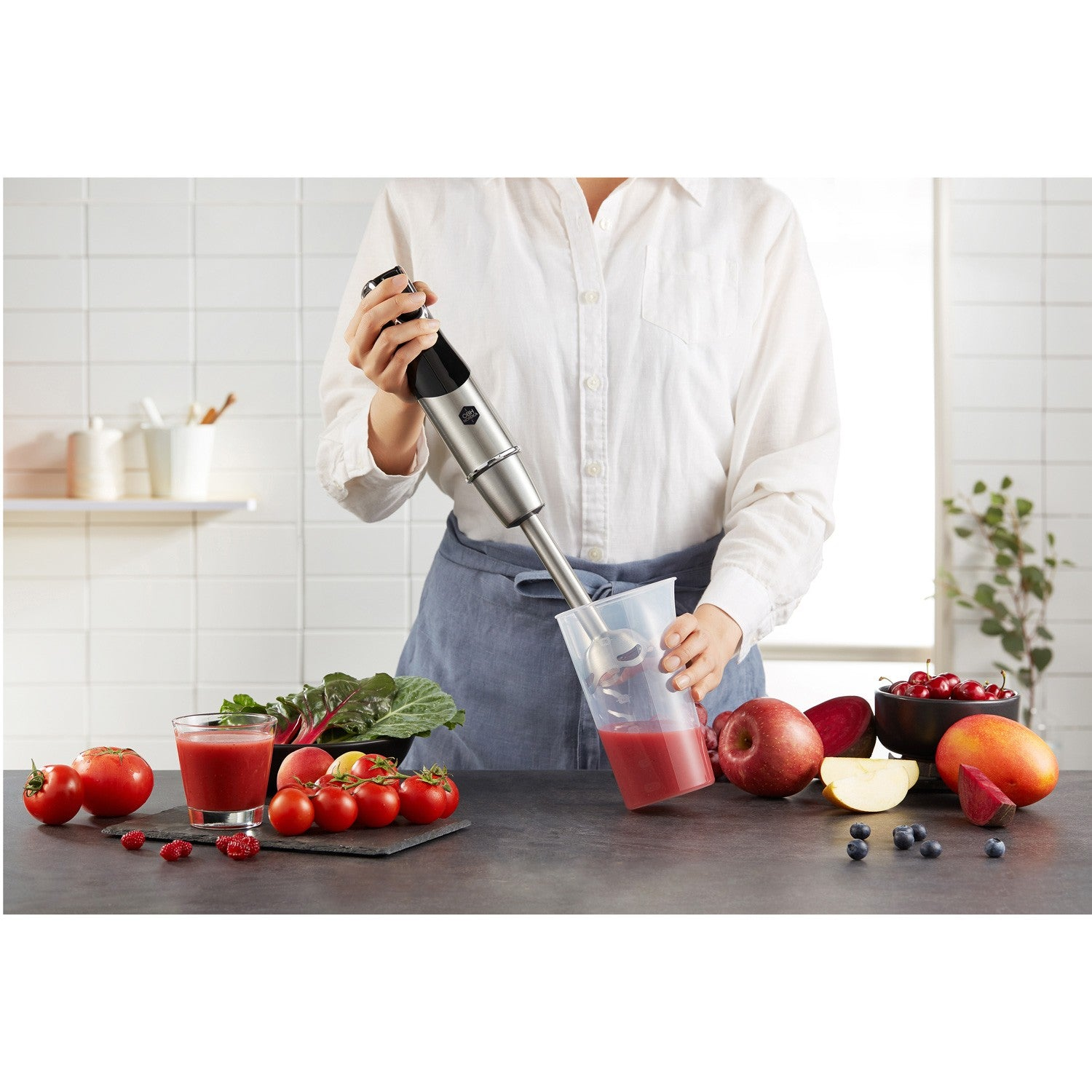 Een persoon mixt rood fruit en groenten in een keuken met een staafmixer.