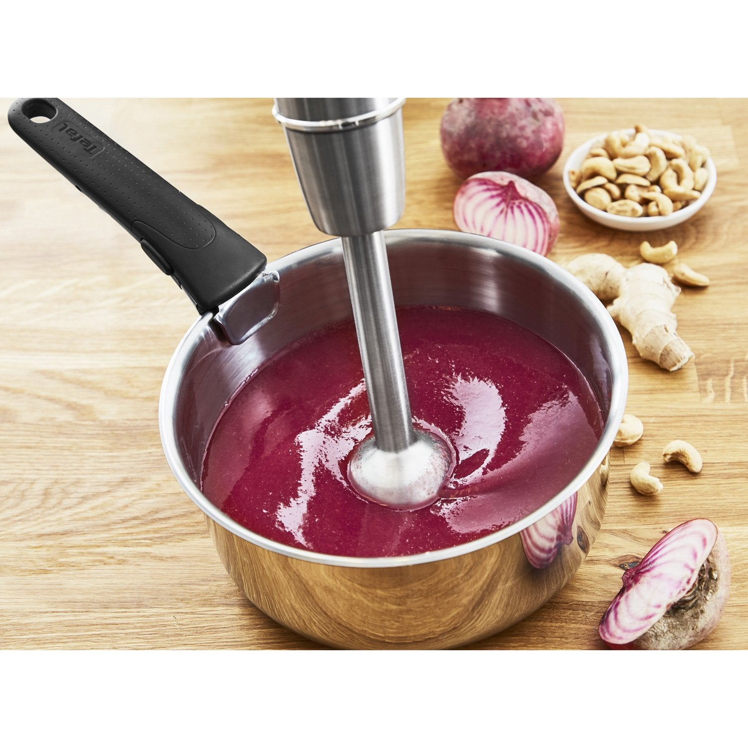 Een staafmixer pureert rode vloeistof in een pan, met rode biet, cashewnoten en gember in de buurt.