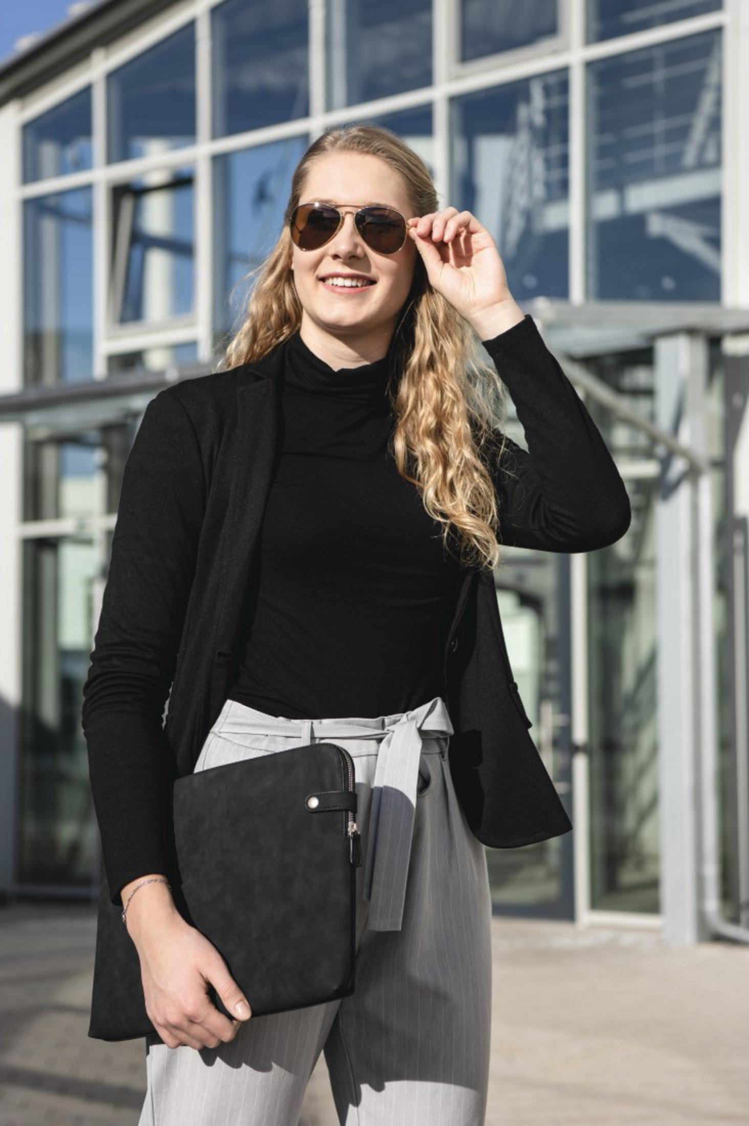 Kobieta z długimi blond włosami nosi czarny golf i kurtkę.