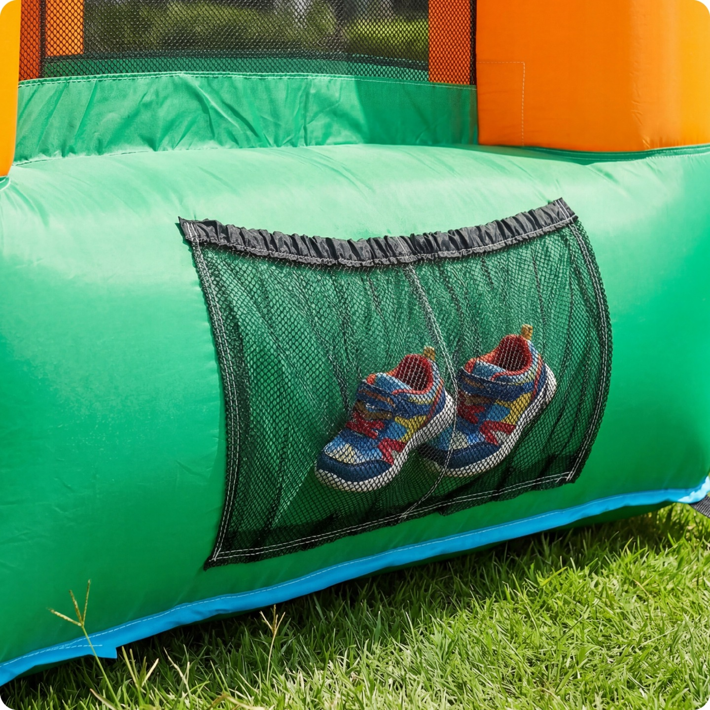Ein Paar bunte Kinderschuhe in einer Netztasche an einer grünen Hüpfburg.