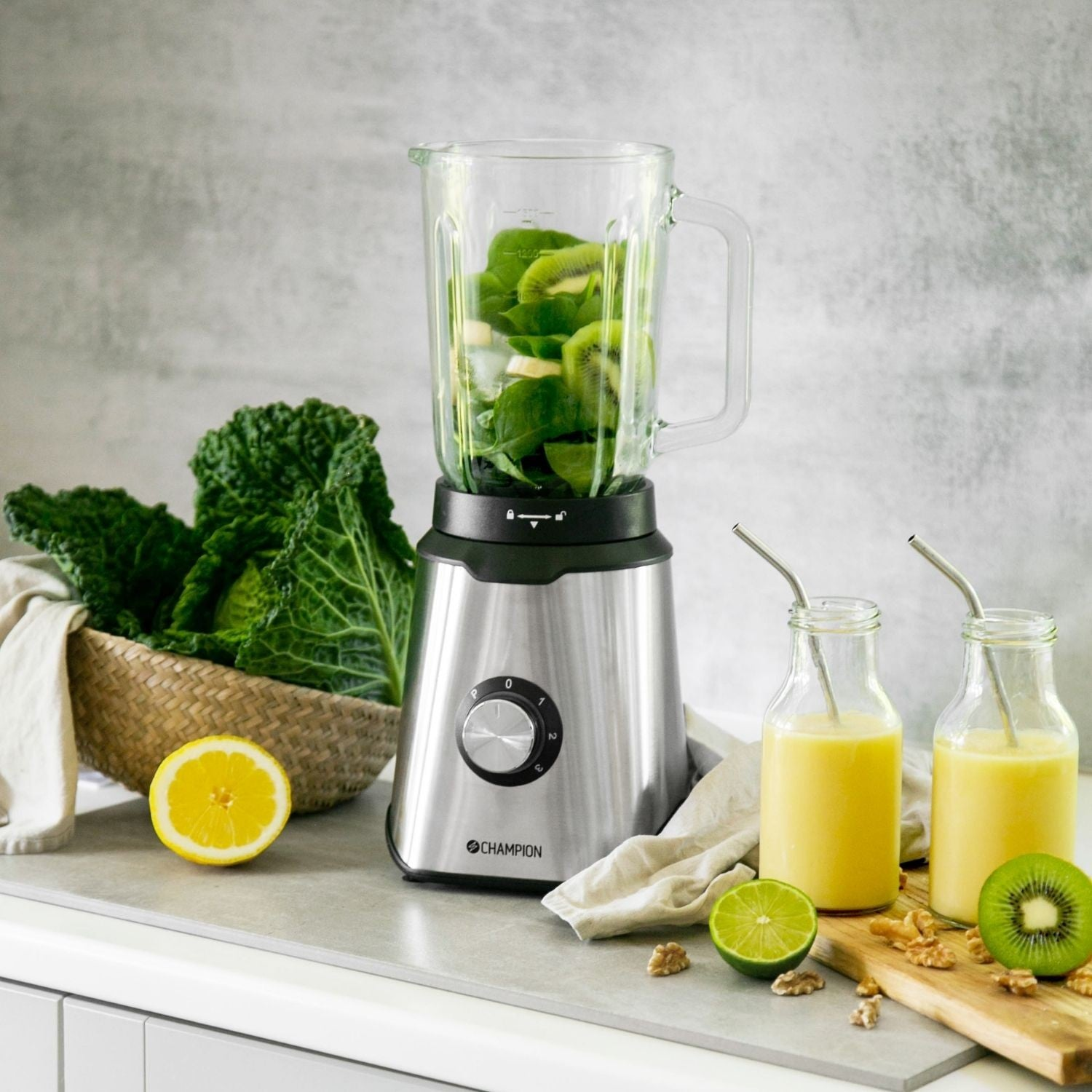 A blender with green smoothie ingredients, next to two bottles of juice.