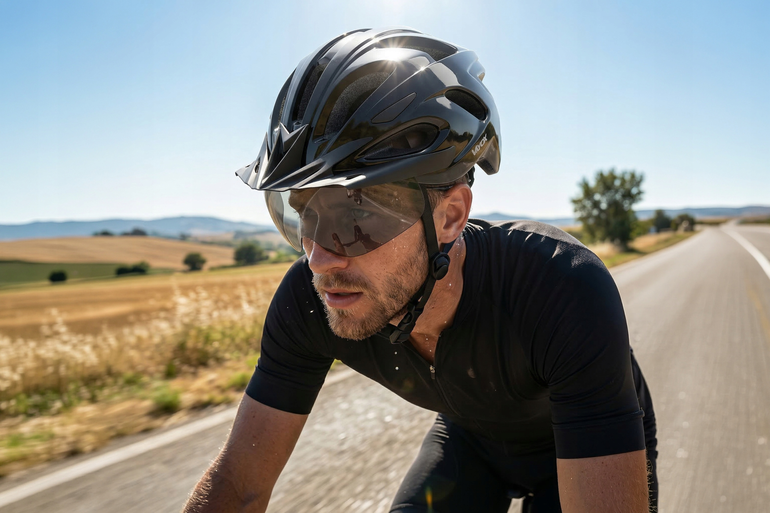 Kolarz nosi czarny kask i okulary przeciwsłoneczne na drodze na zewnątrz.