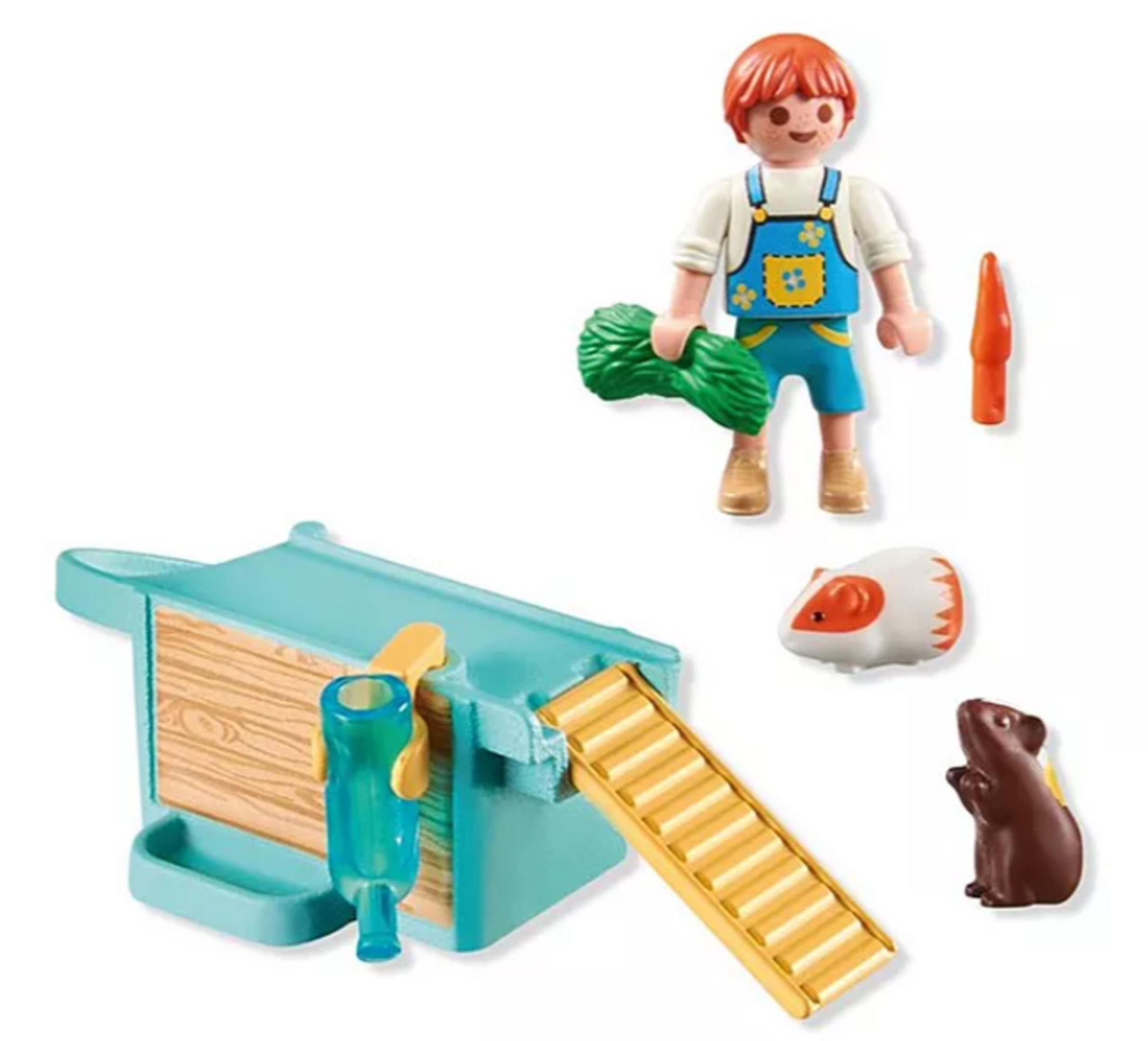 Chłopiec w ogrodniczkach trzyma zielone jedzenie obok klatki dla chomika z rampą i dwoma chomikami.