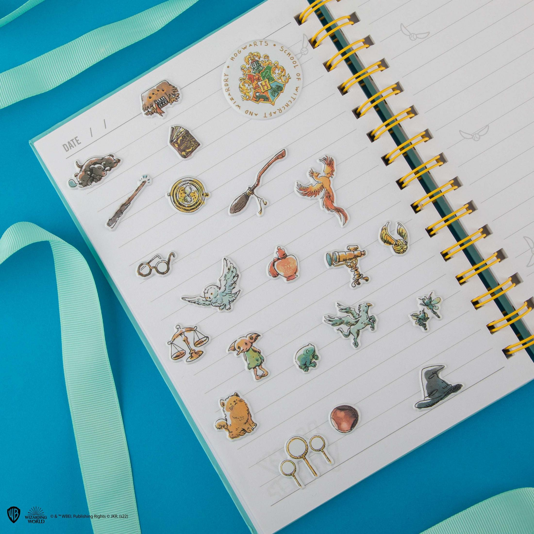 Page de carnet avec autocollants Harry Potter : blason Poudlard, baguette, balai, phénix, hibou, chapeau.