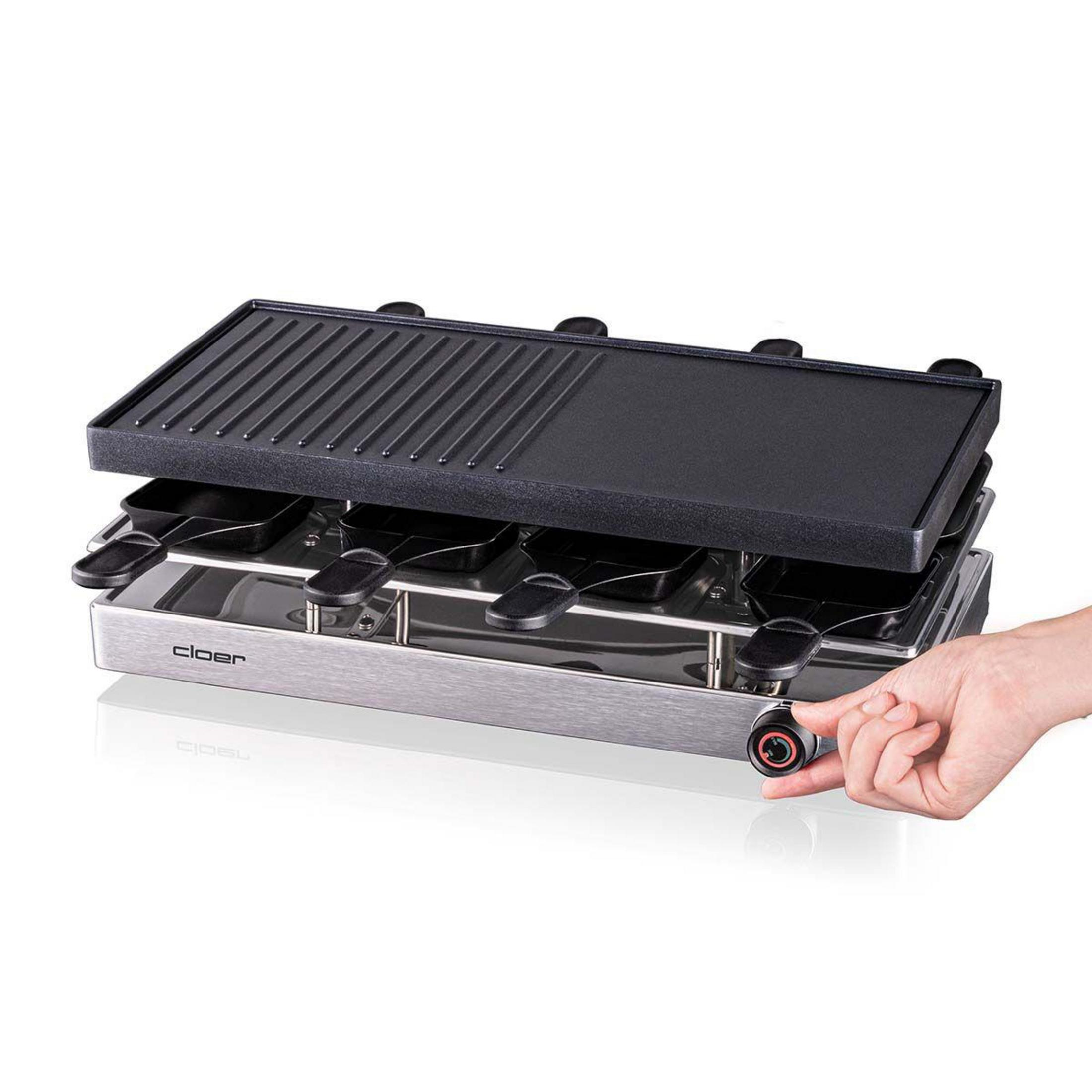 Una griglia per raclette con piastra e padelle; un dito gira la manopola.