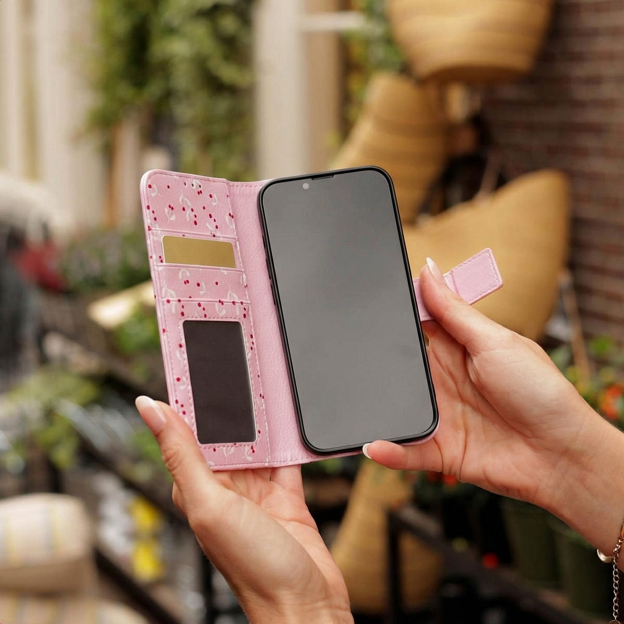 Een persoon houdt een roze telefoonhoesje met kersenpatroon en kaartsleuven vast.