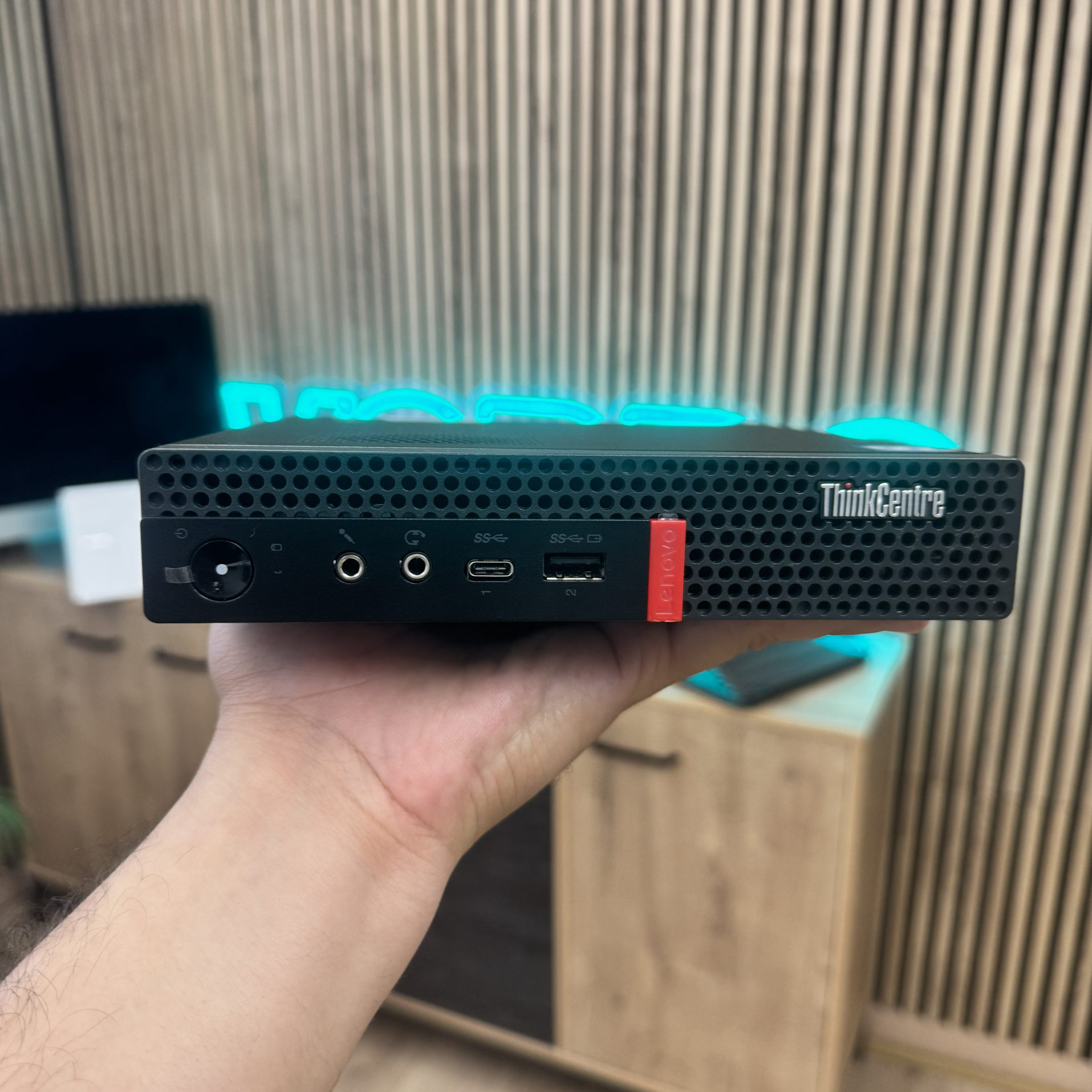 Un mini PC Lenovo ThinkCentre sostenido en la mano. Se ven puertos y rejilla de ventilación.