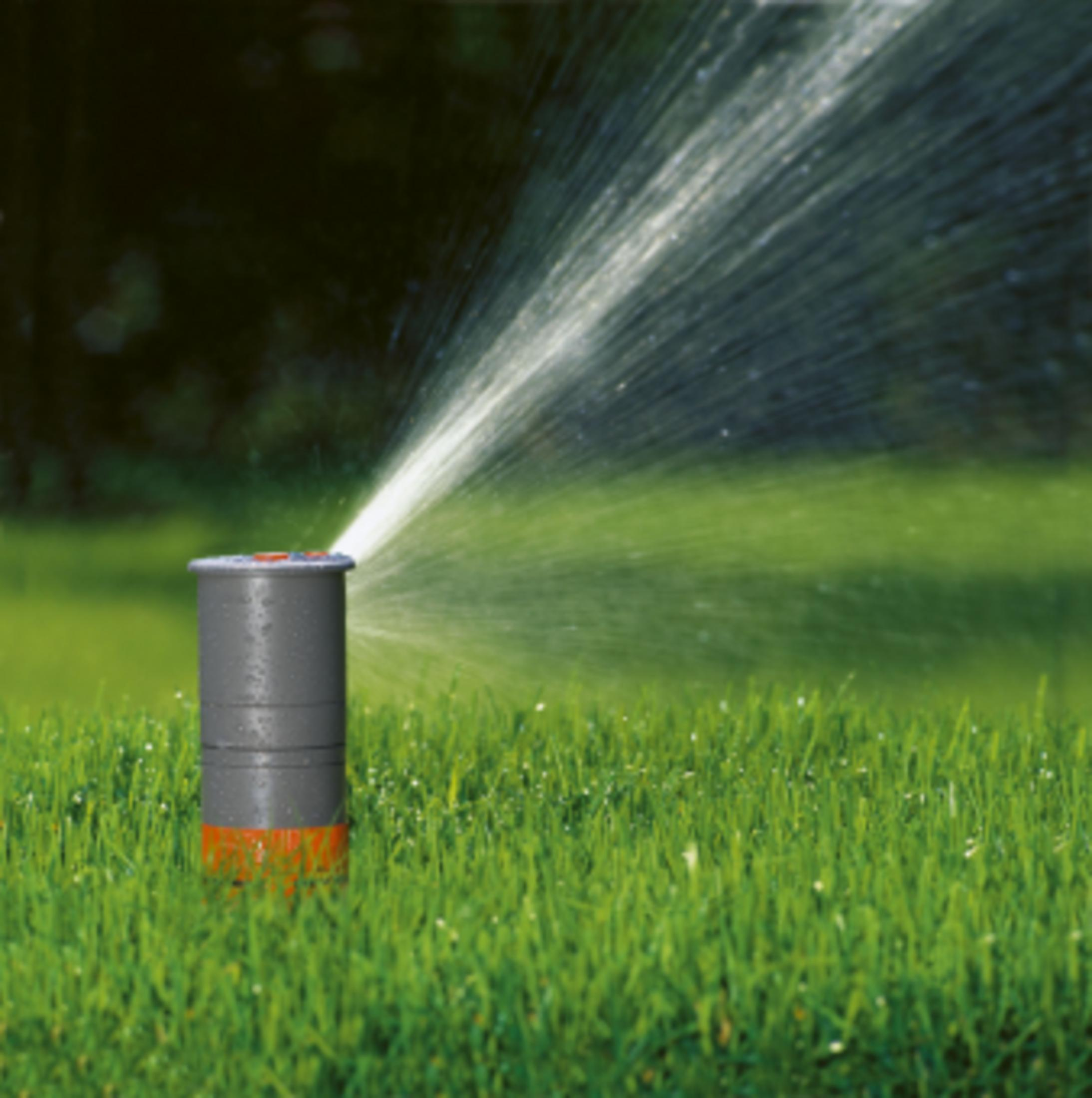 Un irrigatore spruzza acqua sull'erba verde. Sfondo scuro.