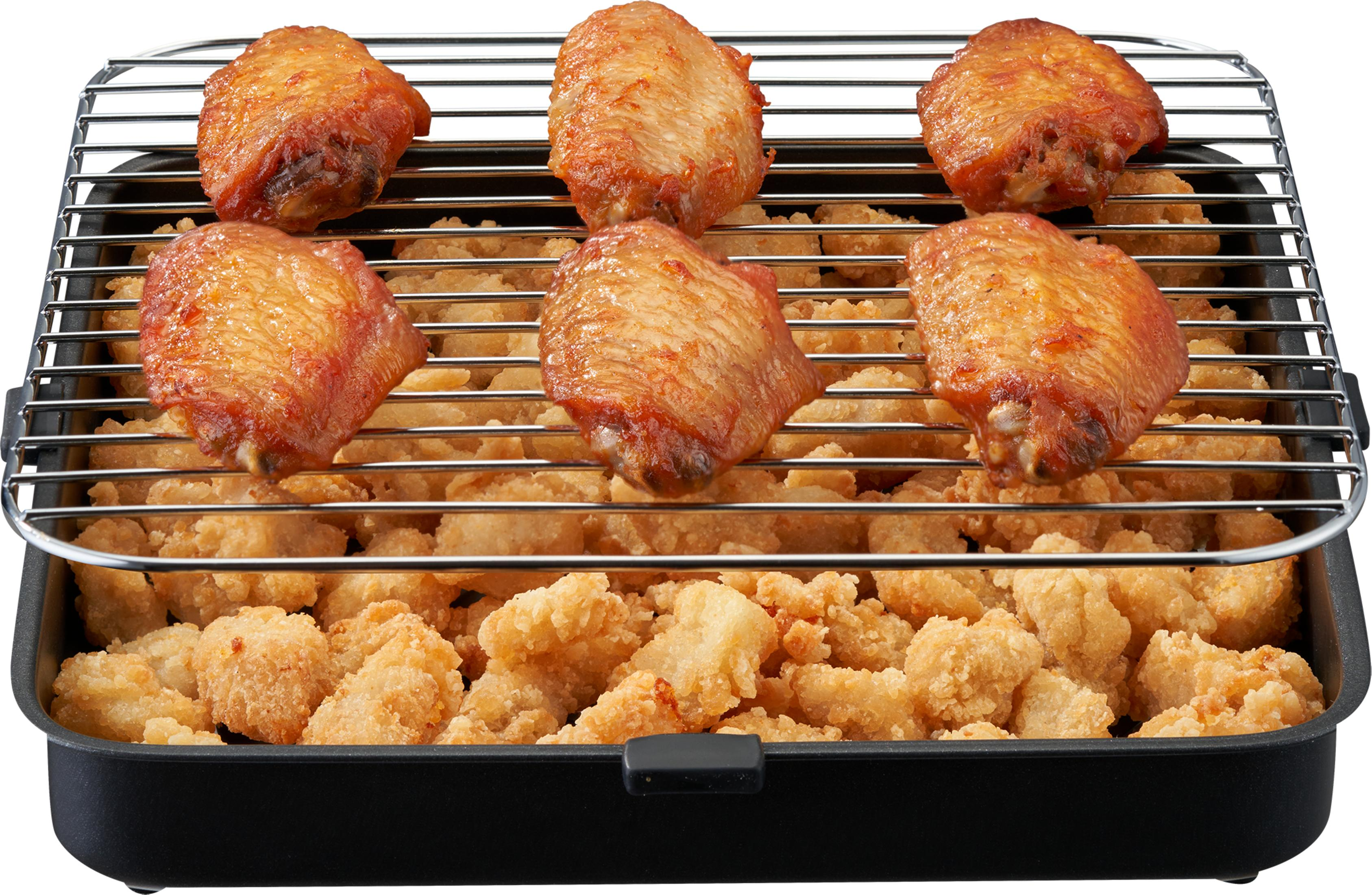 Sześć złocistobrązowych skrzydełek kurczaka na ruszcie nad chrupiącymi nuggetami w czarnej patelni.