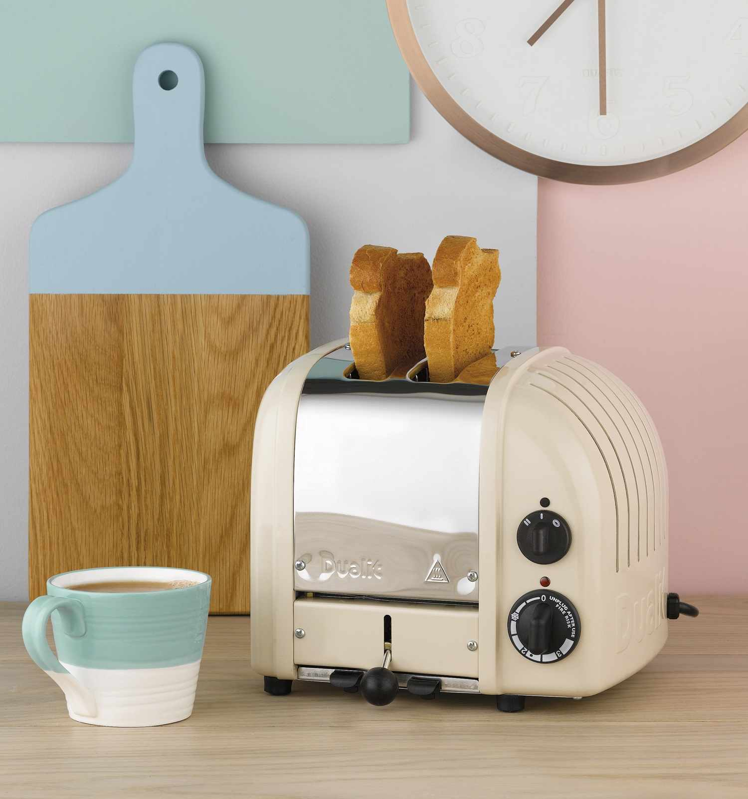 Ein cremefarbener Toaster mit zwei Scheiben Toast, daneben eine Tasse und ein Schneidebrett.