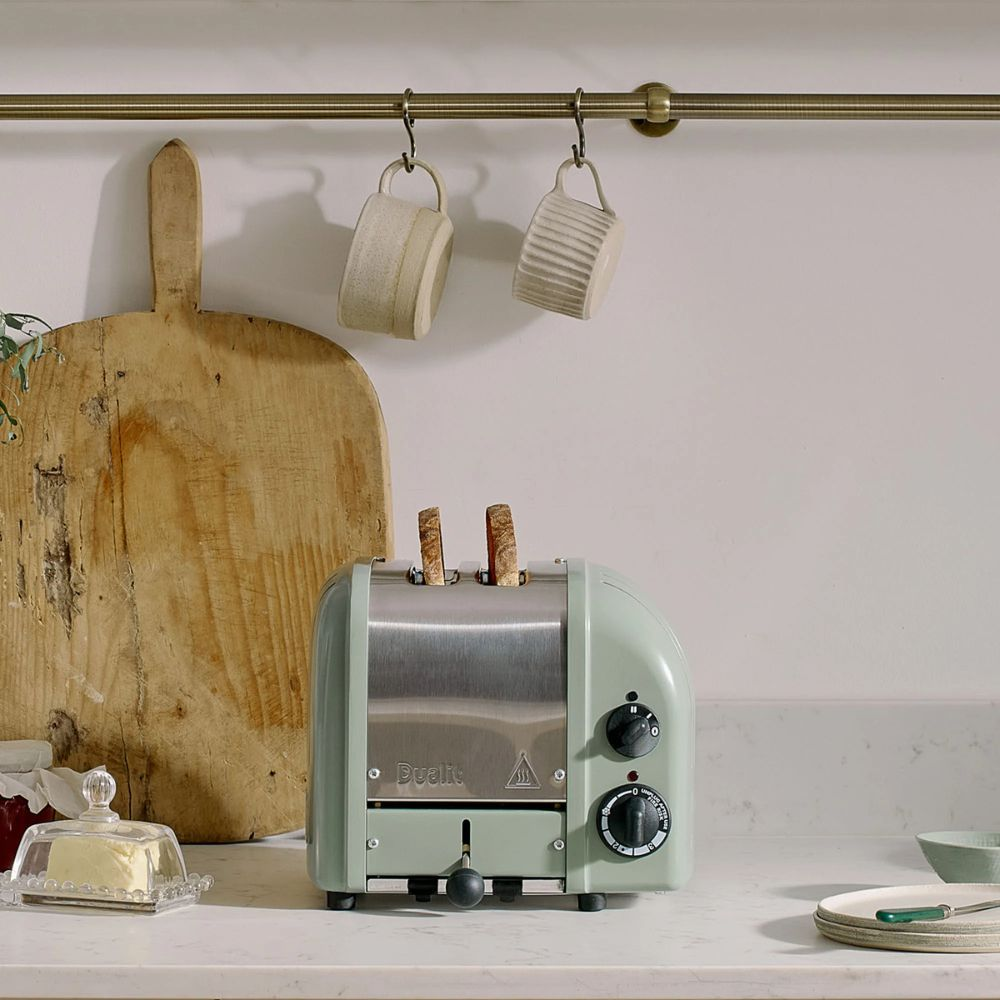 Ein grüner Toaster mit zwei Scheiben Brot, daneben ein Buttergericht und ein Holzbrett.