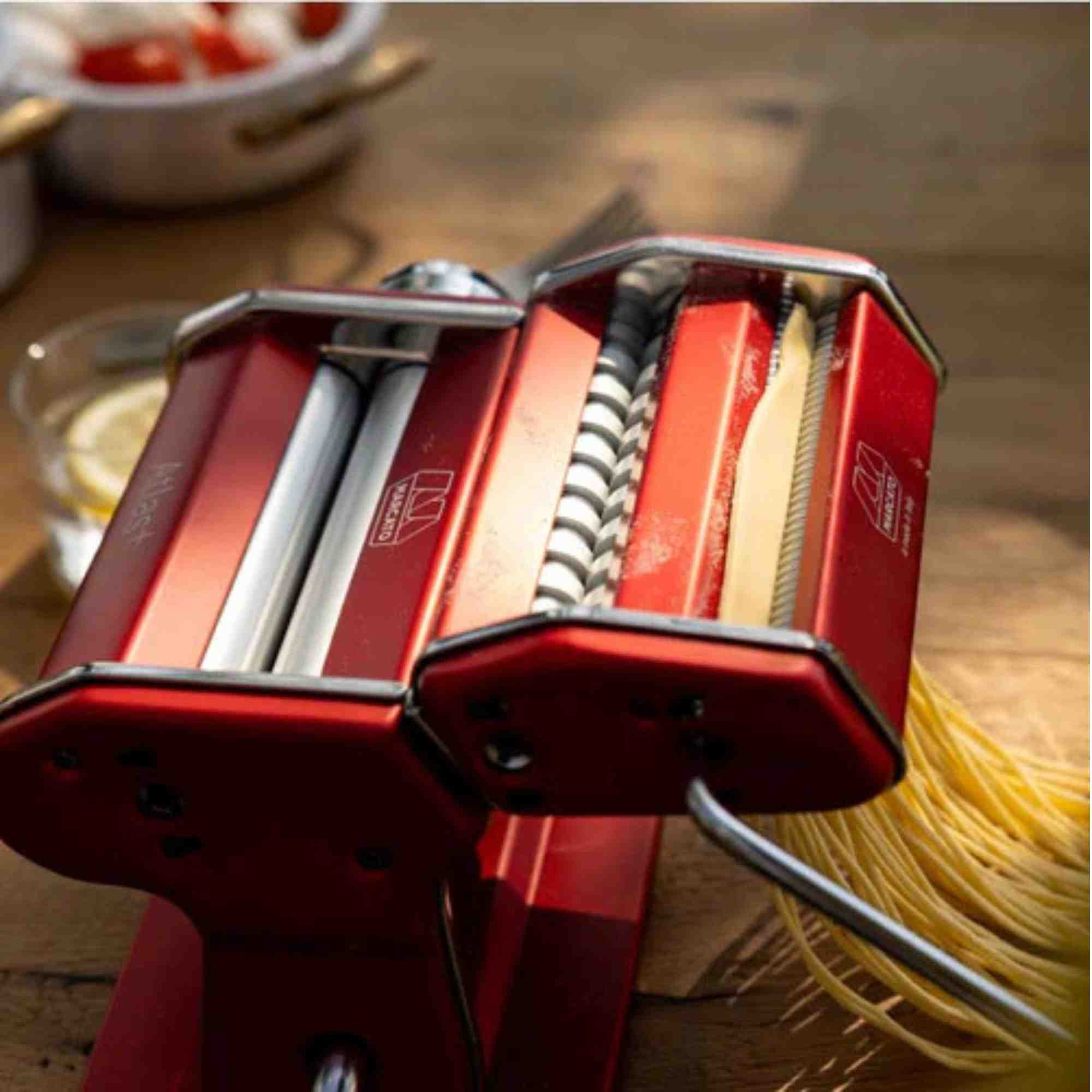 Eine rote Nudelmaschine auf einem Holztisch mit frisch zubereiteten Spaghetti.