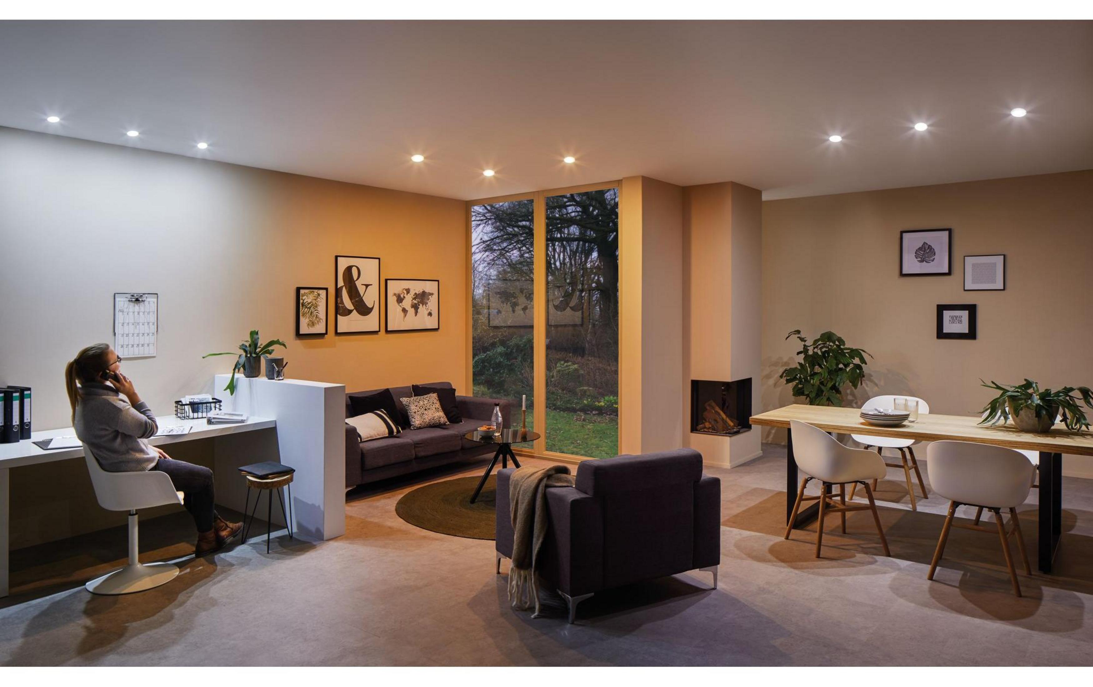 Moderne Wohnküche mit Frau am Schreibtisch, Sofa, Esstisch und Kamin.