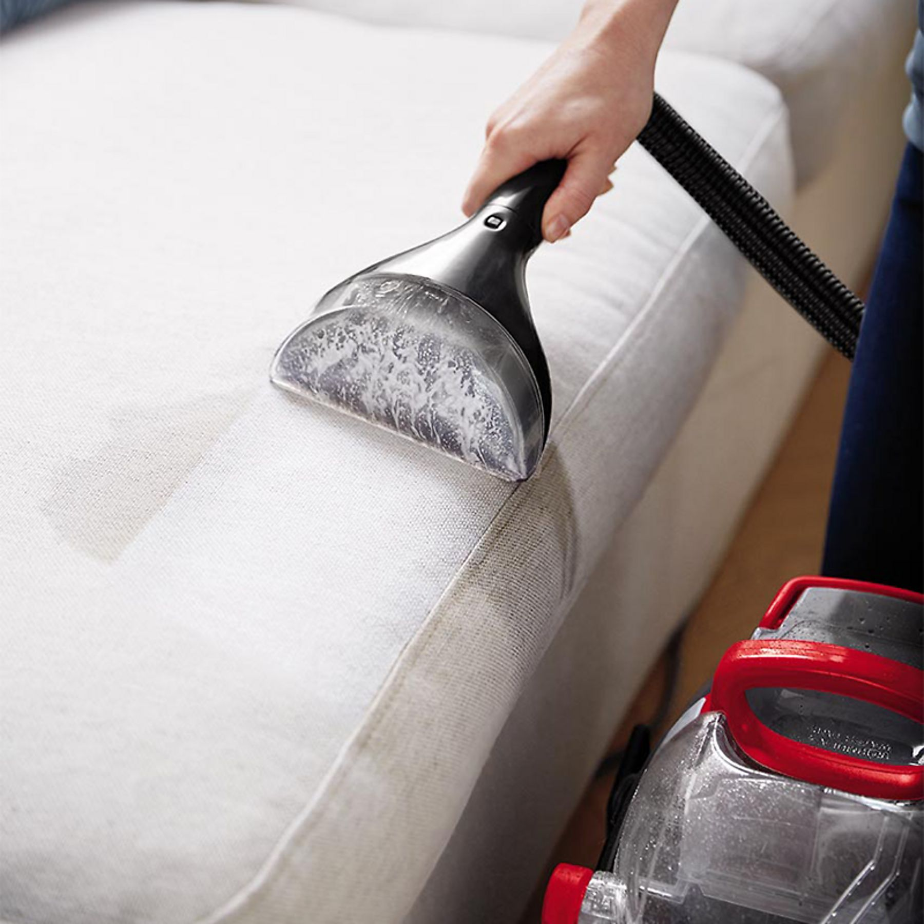 Ręka używa czyścika do tapicerki na białej kanapie.