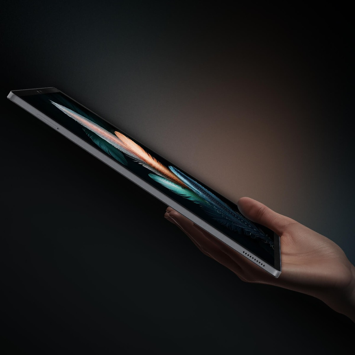 Una mano tiene un tablet elegante con immagine di piuma su sfondo scuro.