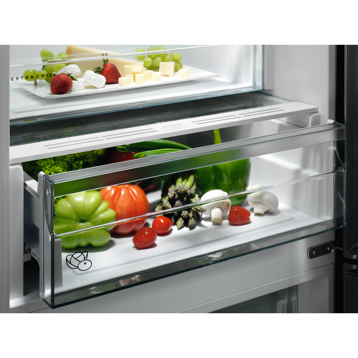 Un cajón de refrigerador con frutas y verduras frescas como uvas, fresas, queso, tomates, pimientos, champiñones y lechuga.