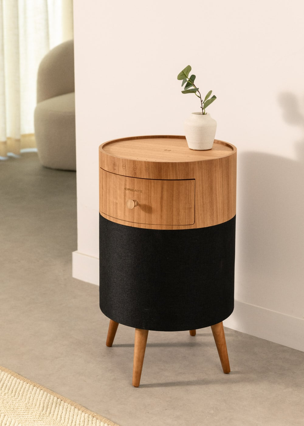 Una mesita de noche redonda de madera con base de tela negra y tres patas.
