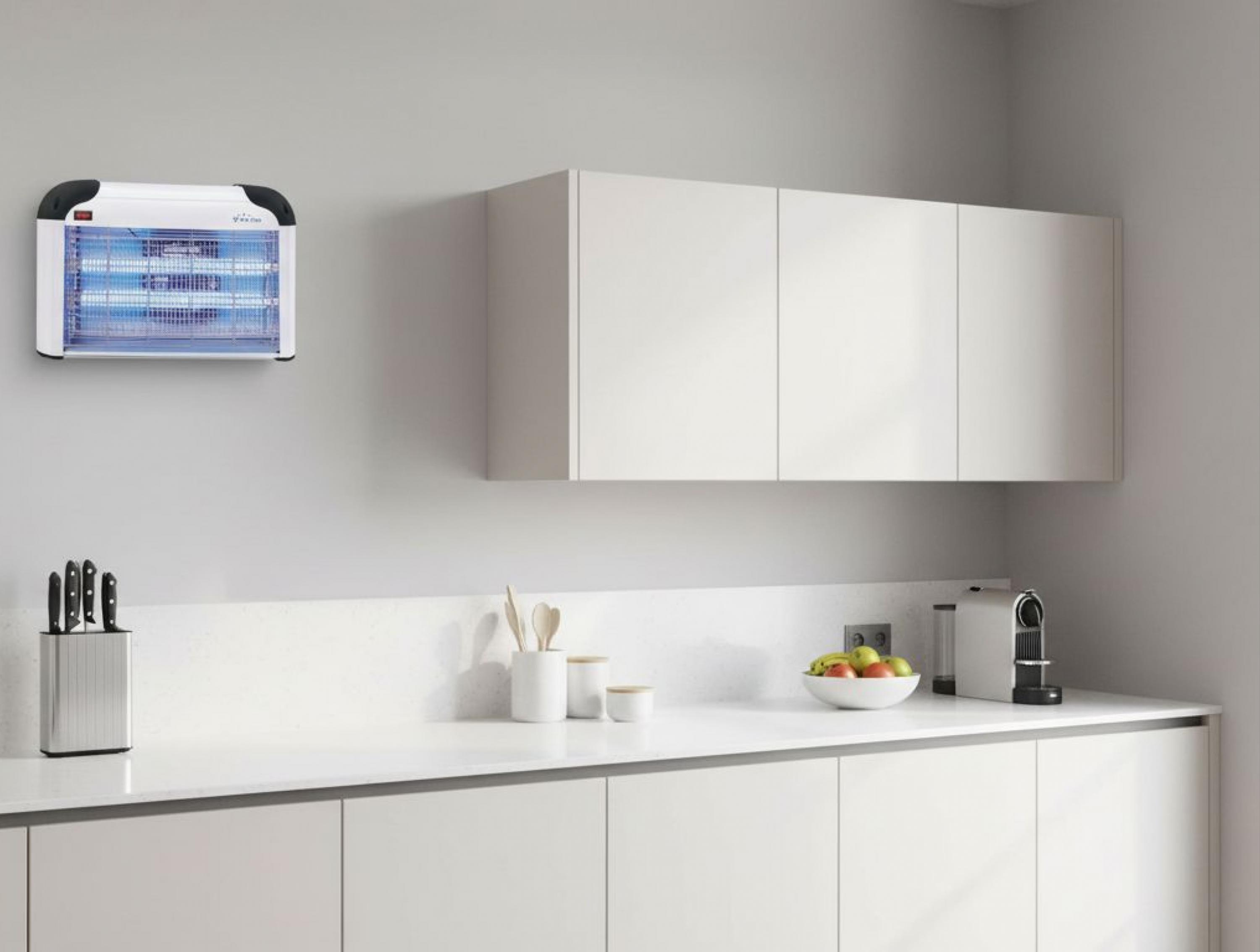 Un mata insectos blanco con luces azules cuelga en una pared gris sobre una encimera de cocina blanca.
