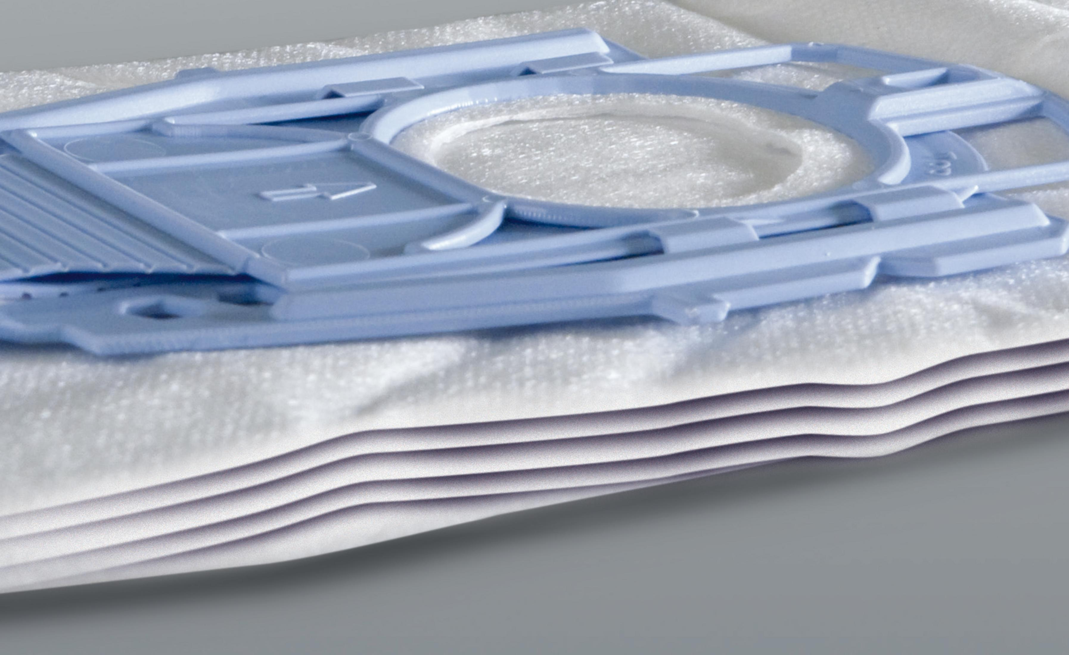 Ein blauer Plastikadapter liegt auf einem Stapel weißer Staubsaugerbeutel.