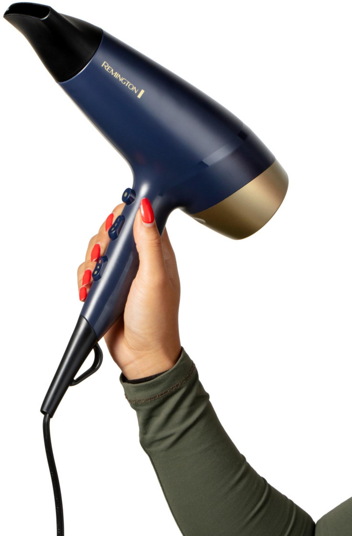 Dłoń z czerwonymi paznokciami trzyma ciemnoniebieską suszarkę Remington ze złotym akcentem.