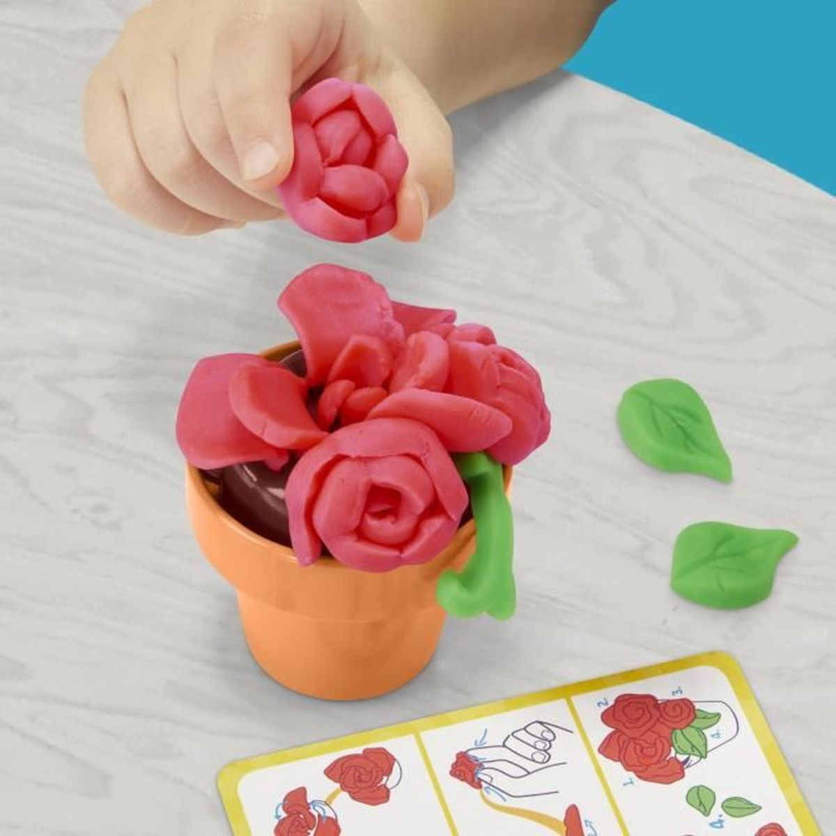 Un niño moldea una rosa roja de plastilina para una maceta.