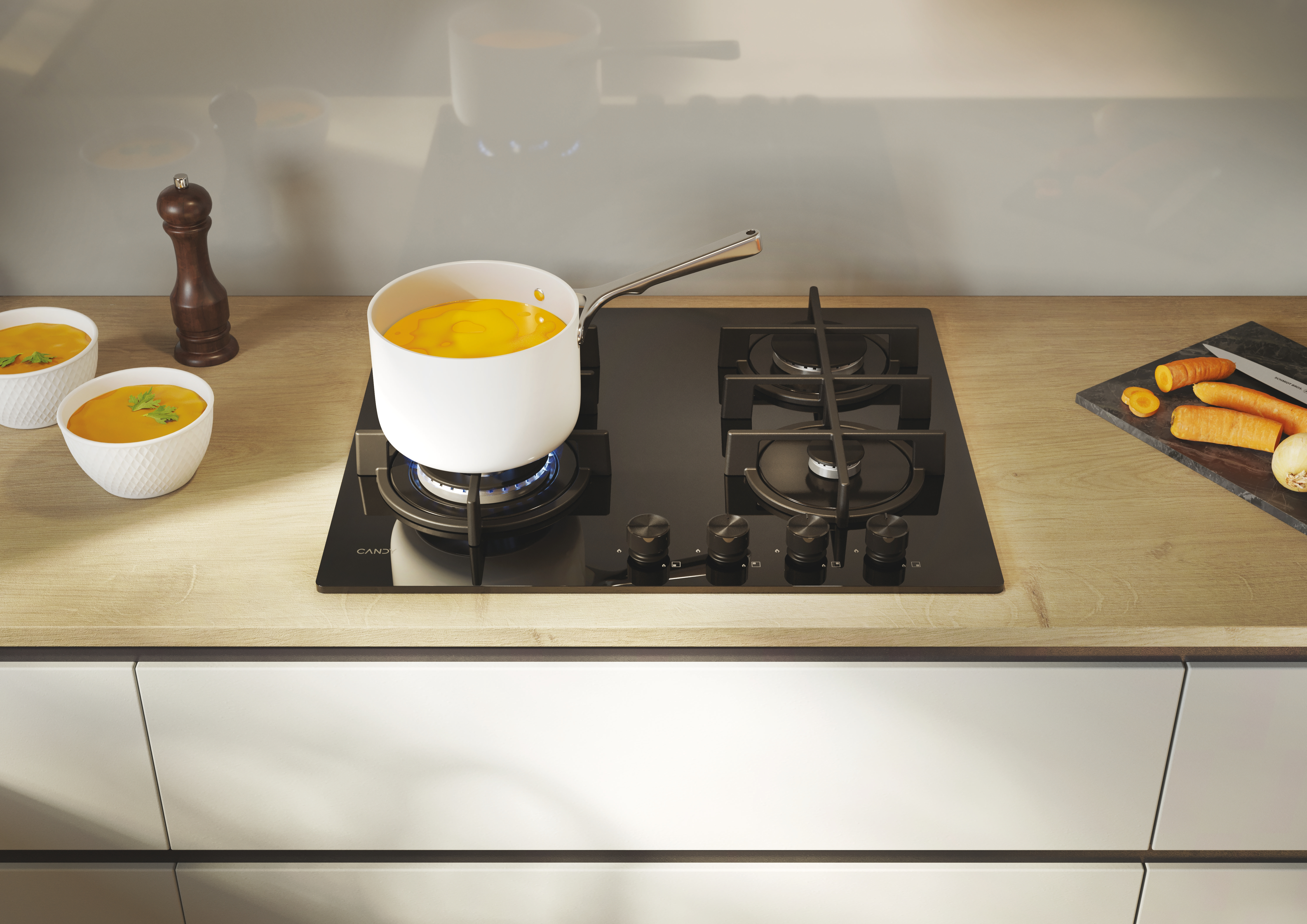 Una olla con líquido amarillo se cocina en una estufa de gas, con cuencos y zanahorias cerca.