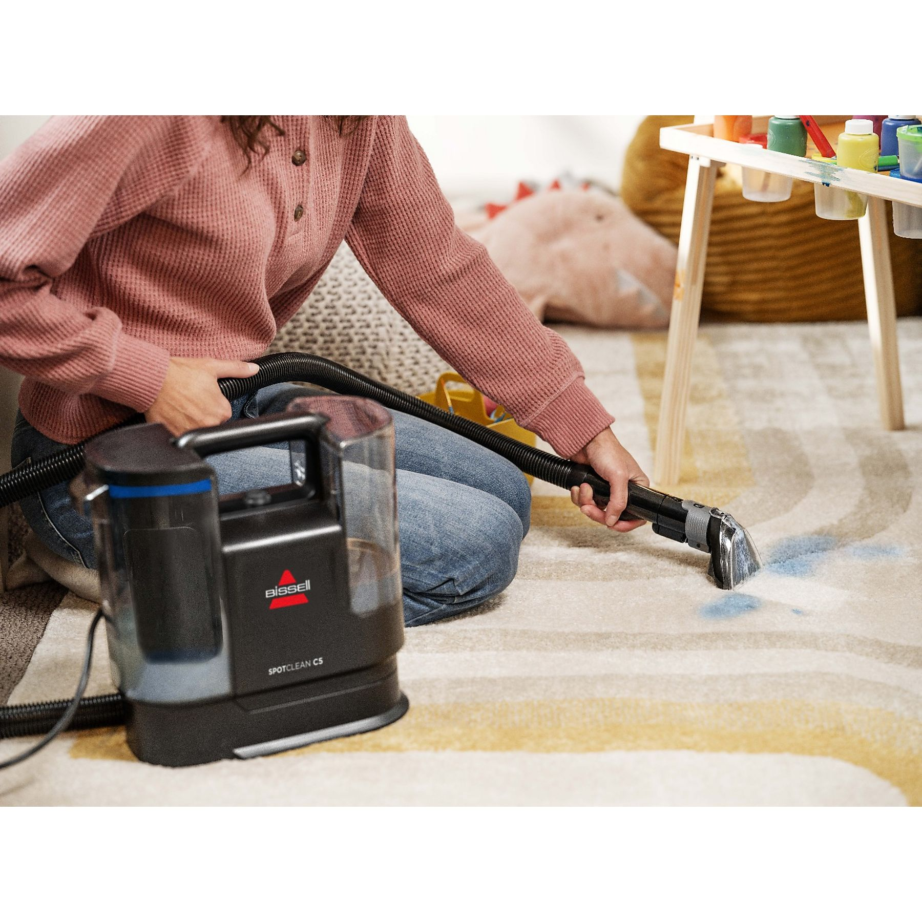 Eine Person reinigt mit einem Bissell Spotclean C5 Teppichreiniger einen Teppich mit Flecken.