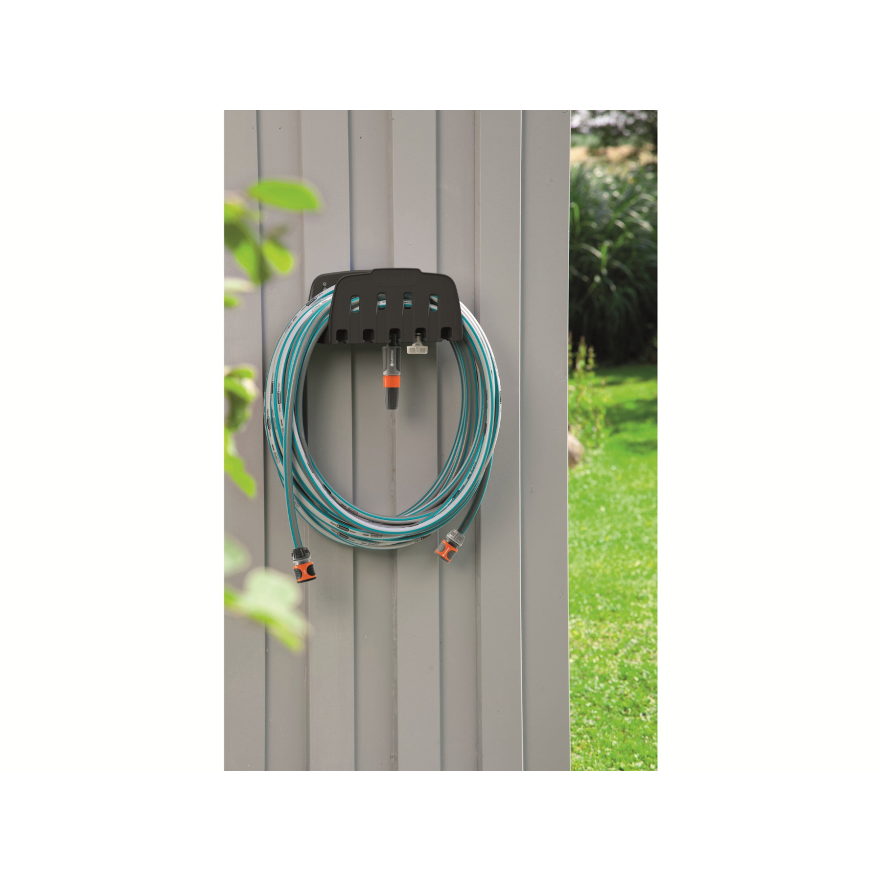 Schlauchaufroller mit Schlauch an grauer Wand, Garten im Hintergrund.