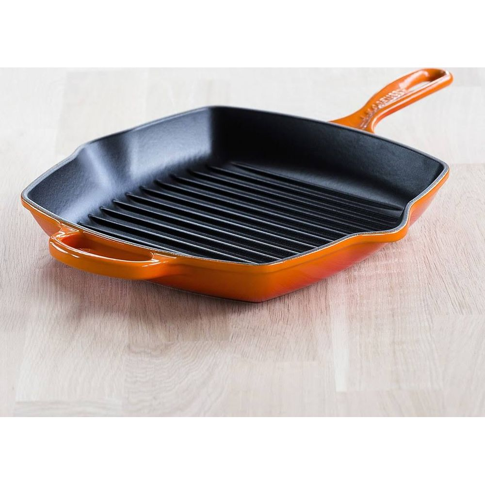 Eine orangefarbene Grillpfanne mit schwarzen Rillen auf einem Holztisch.
