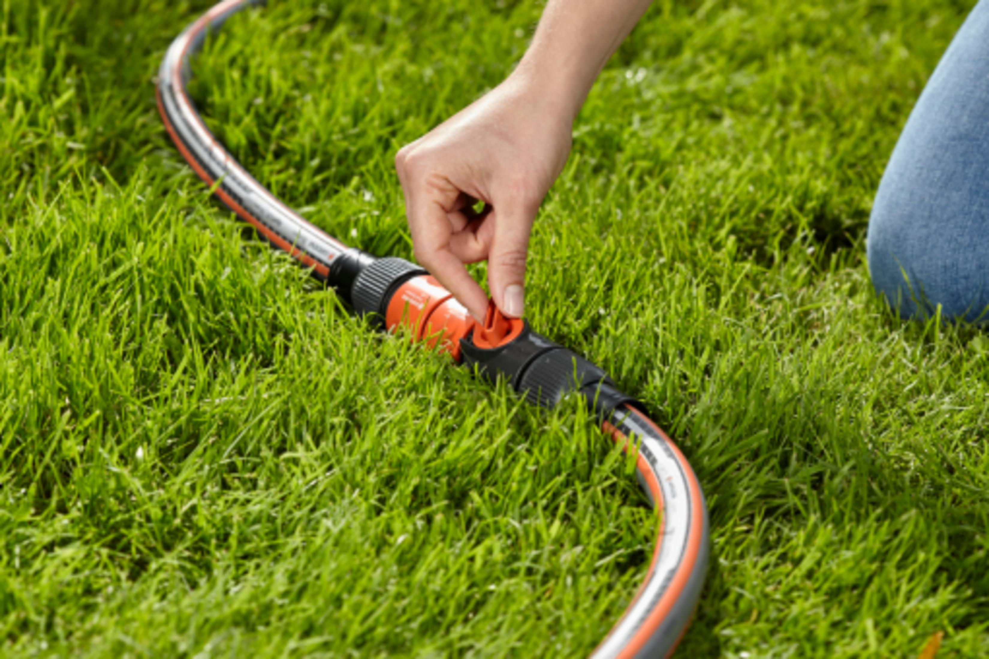 Hand stelt rode hendel van tuinslang op groen gras in.