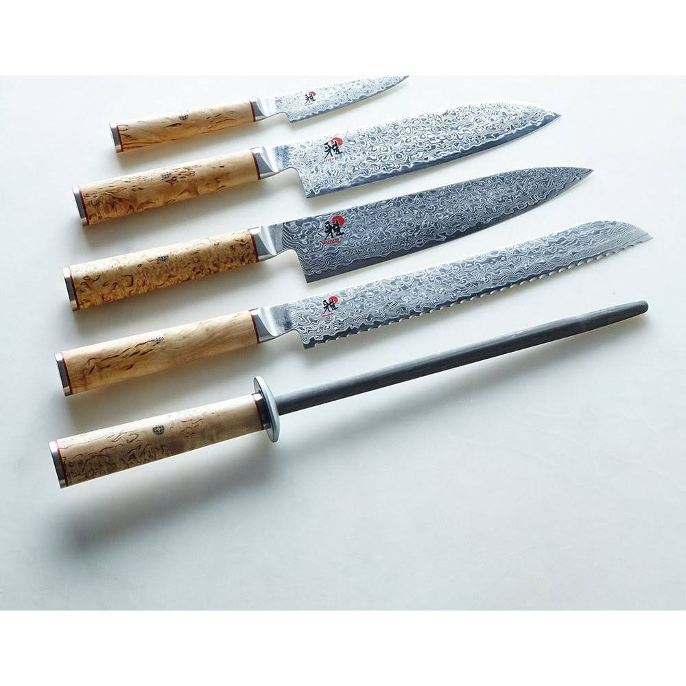 Pięć noży ze stali damasceńskiej i stal do ostrzenia ułożone po przekątnej na białej powierzchni.