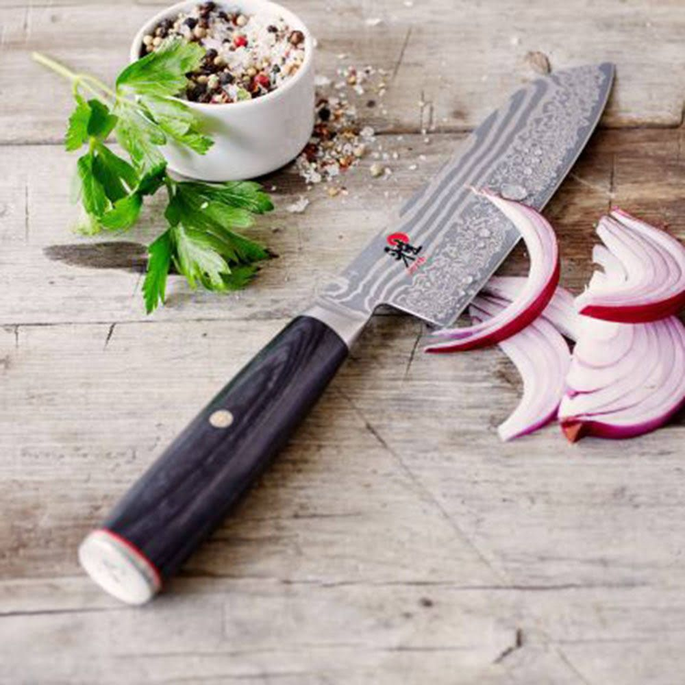 Nóż damasceński leży obok krążków czerwonej cebuli i małej miseczki z przyprawami.