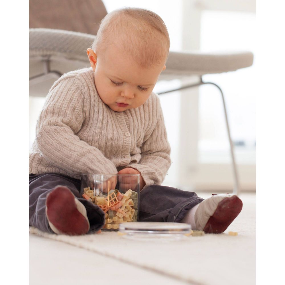 Bambino seduto su tappeto gioca con pasta in barattolo.